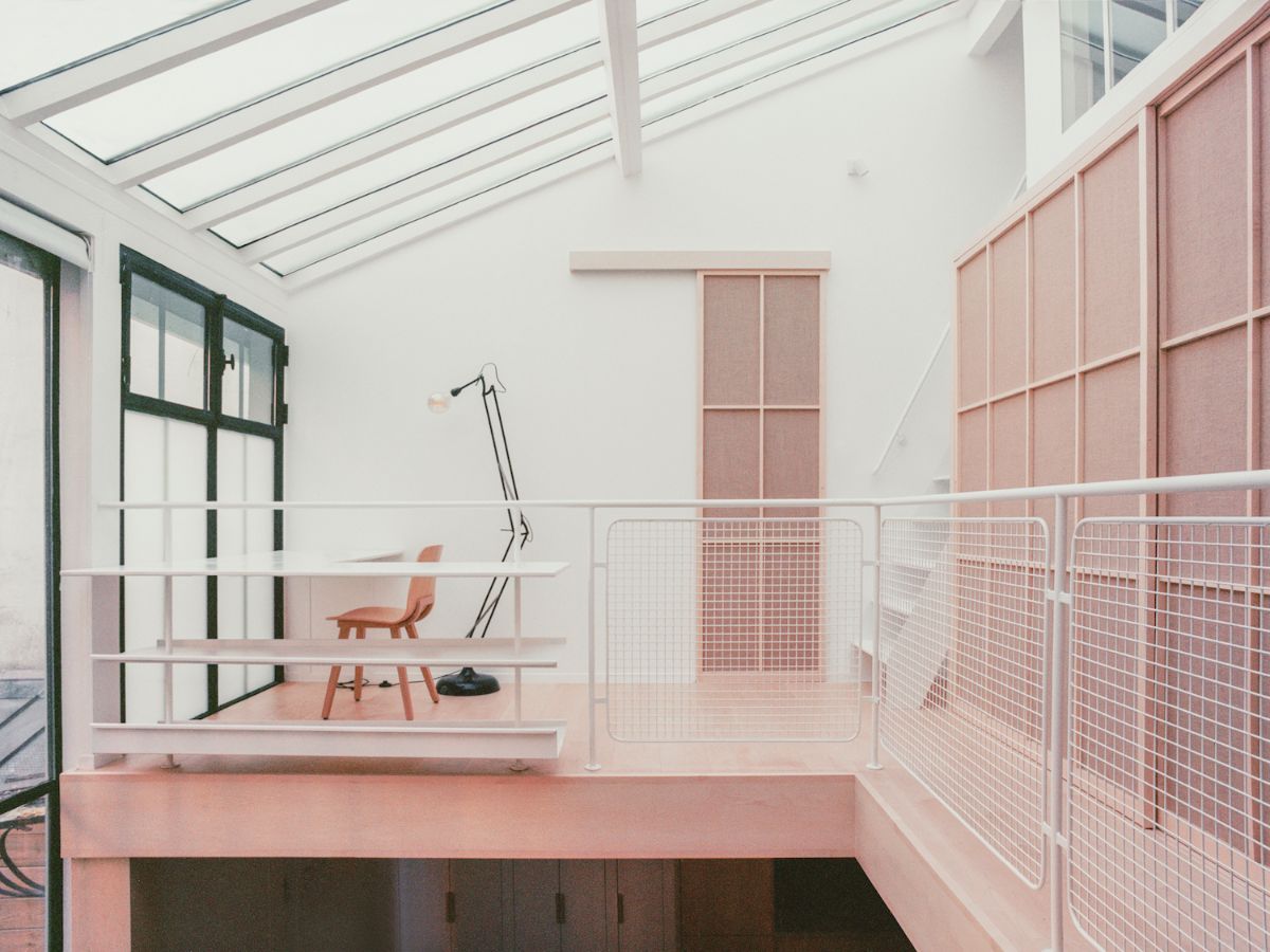 Jean Moulin Atelier – House by Atelier NEA — A mezzanine studio space bathed in overhead skylight, divided by a white-painted open shelving unit with integrated mesh panels.