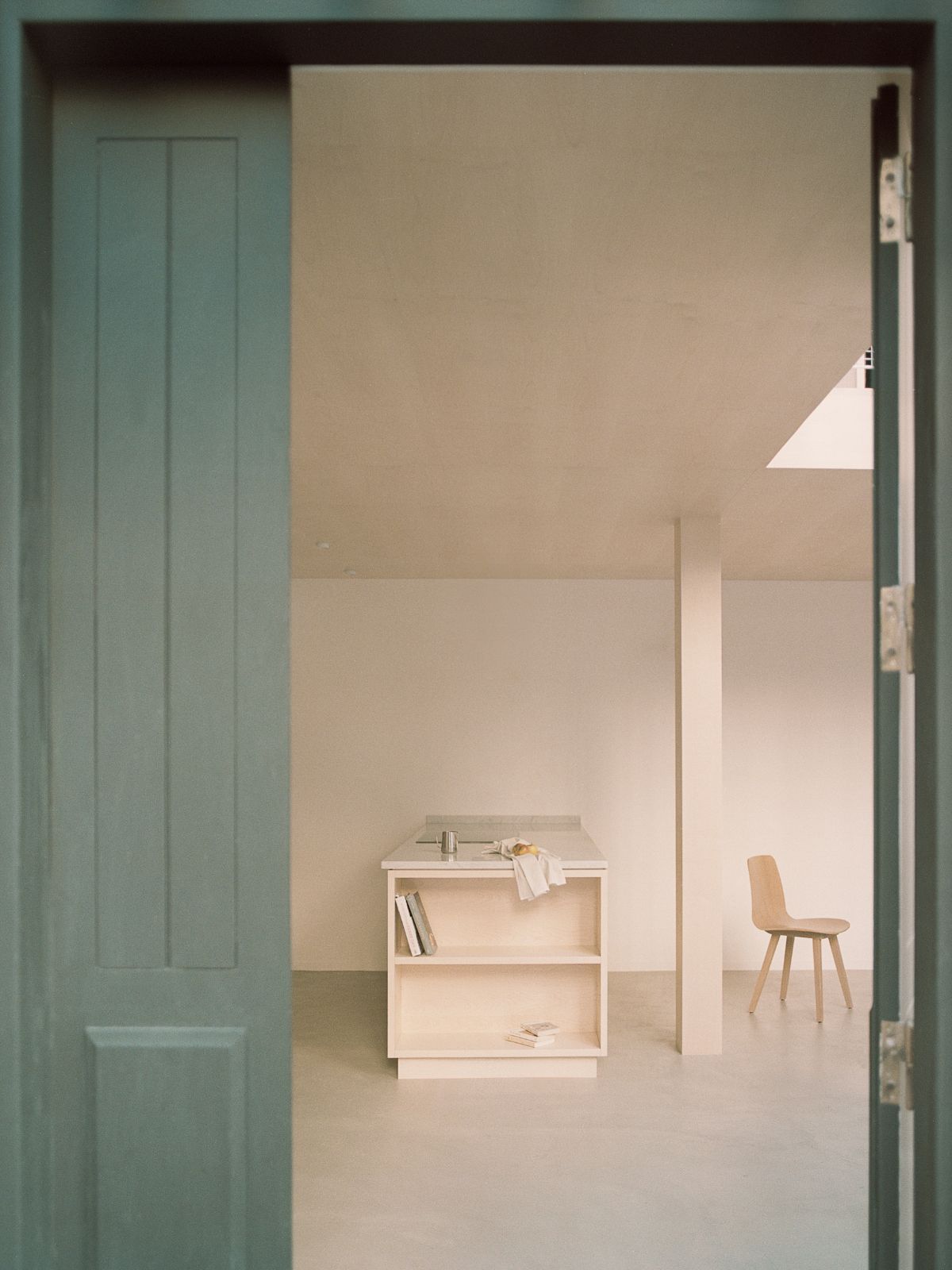 Jean Moulin Atelier – House by Atelier NEA — View through sage-painted paneled door into the renovated artist studio, framing a precisely composed interior.