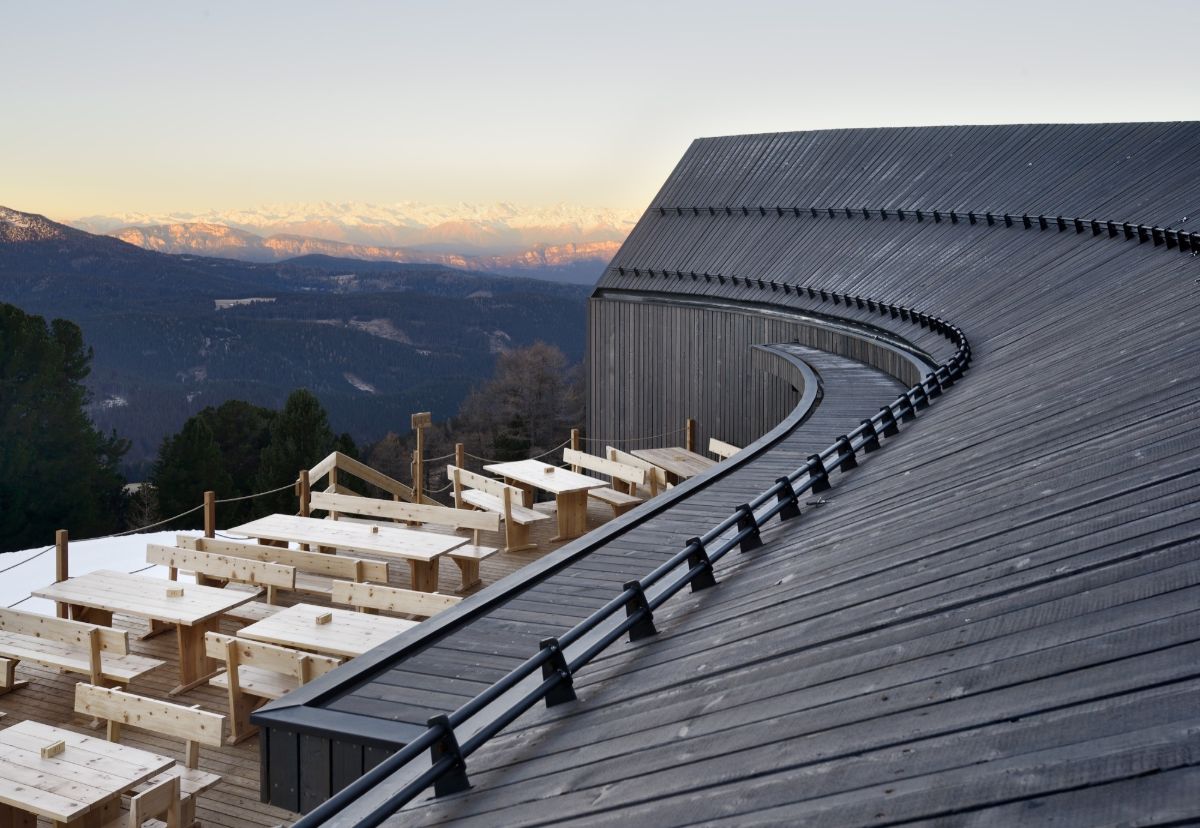 Oberholz Mountain Hut by Peter Pichler & Pavol Mikolajcak by Peter Pichler Architecture — The Oberholz Mountain Hut cantilevers dramatically across a snowy alpine slope, its three connected pavilions defined by pitched-roof volumes clad in dark...