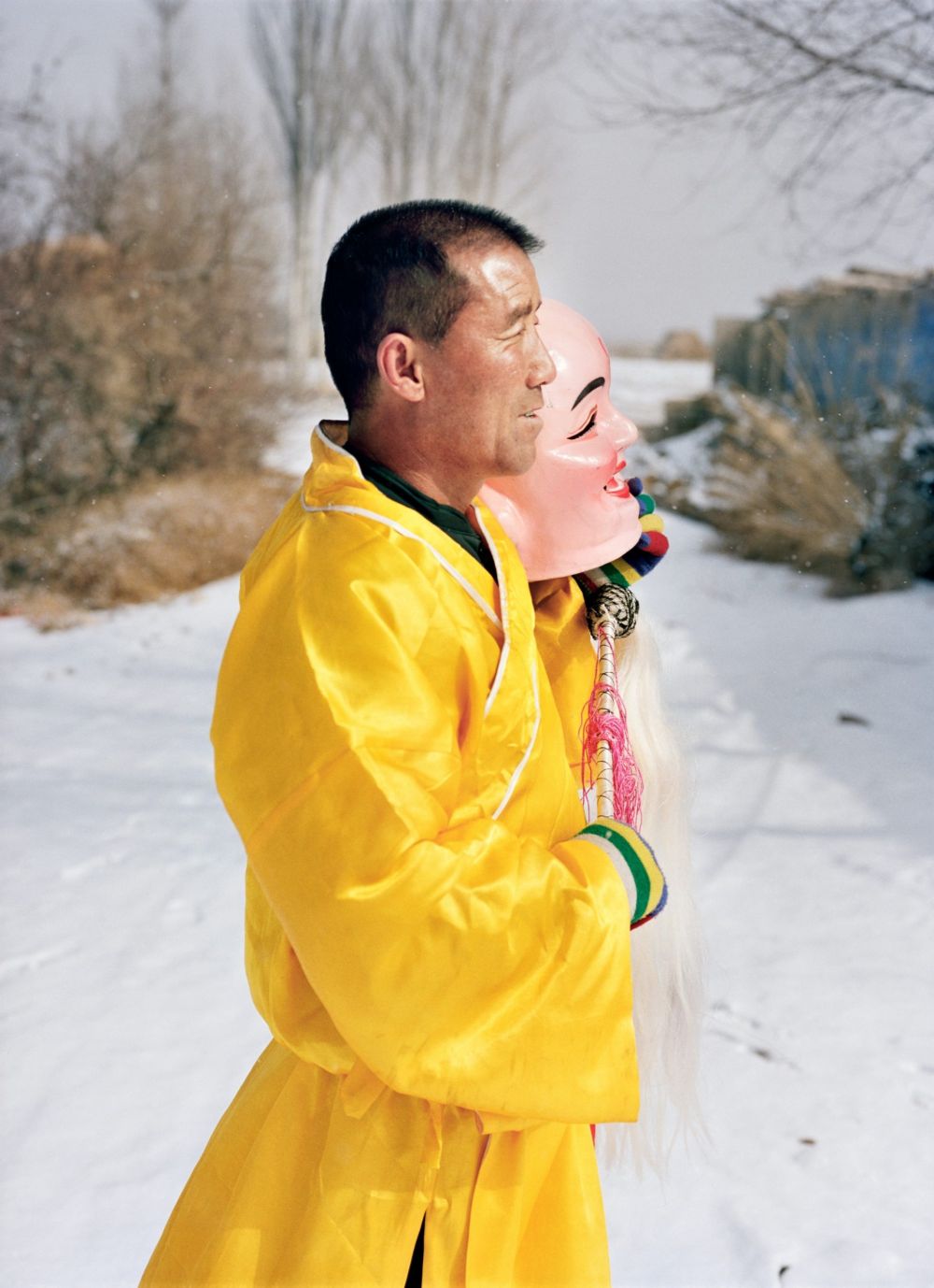 Watering My Horse by Xiaoxiao Xu — A man in a vivid yellow jacket holds an inflatable pink mask depicting a smiling female face against the Ming dynasty stone wall section.