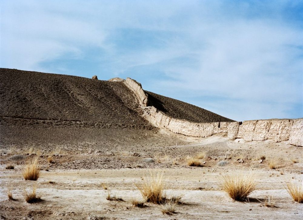 Watering My Horse by Xiaoxiao Xu — A section of Ming dynasty stone masonry wall curves across an arid hillside, its rectangular blocks stacked in horizontal courses with visible crenellations...