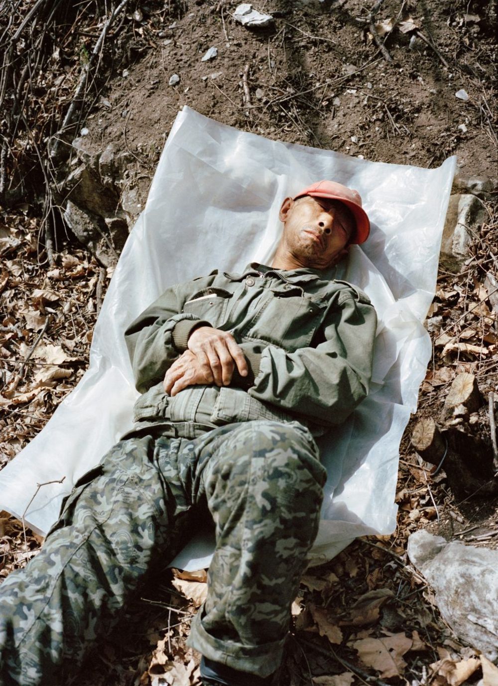 Watering My Horse by Xiaoxiao Xu — A soldier in olive drab fatigues and rust-red cap lies supine on white fabric laid across rocky, debris-strewn ground at the Great Wall's Ming dynasty ruins.