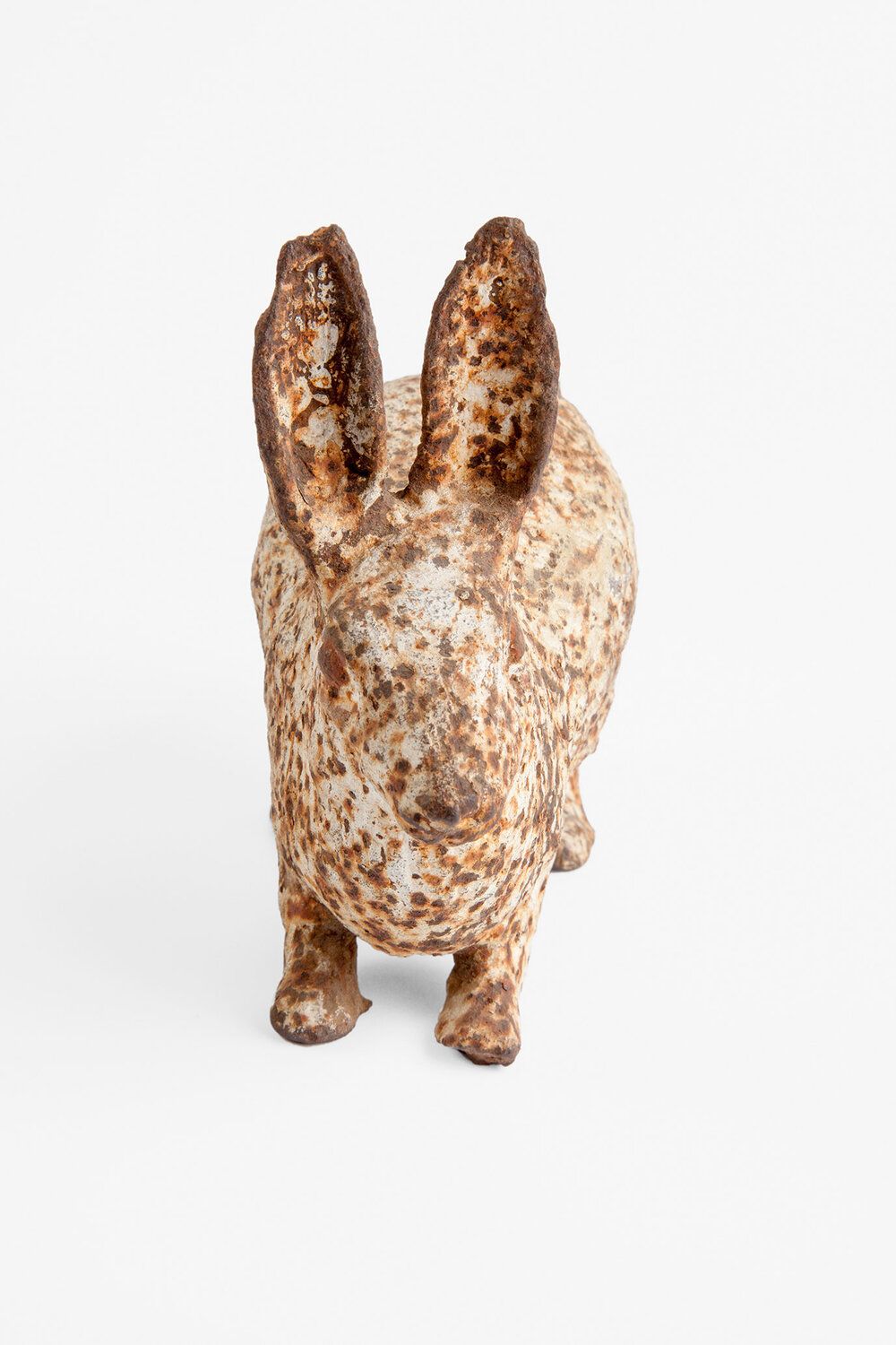 Watering My Horse by Xiaoxiao Xu — A terracotta or earthenware figurine of a rabbit stands centered against a white background, its surface covered in rust-colored oxidation and white mineral...