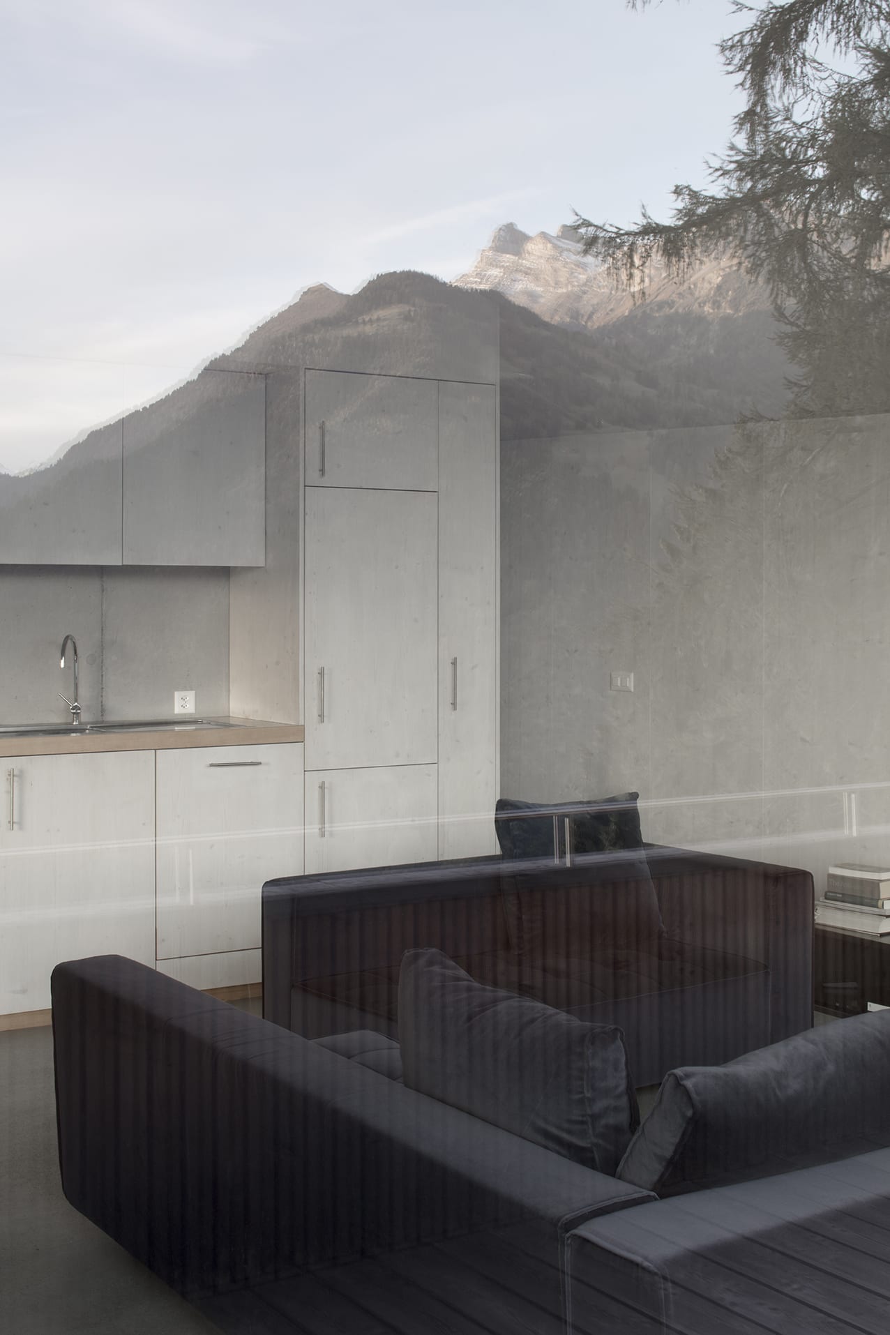 En Chalméry House by Christian Dupraz Architects — A minimalist interior framed by floor-to-ceiling glazed doors with dark steel mullions, revealing a living space anchored by a single black ribbed chair...