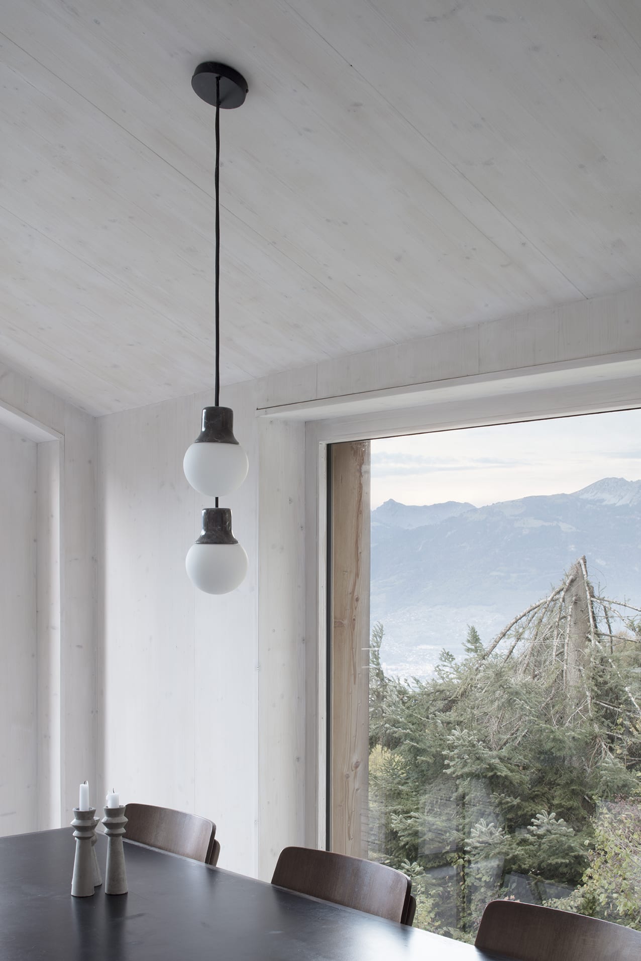 En Chalméry House by Christian Dupraz Architects — A dining space framed by floor-to-ceiling glazed doors with dark steel mullions opening onto an Alpine valley landscape.