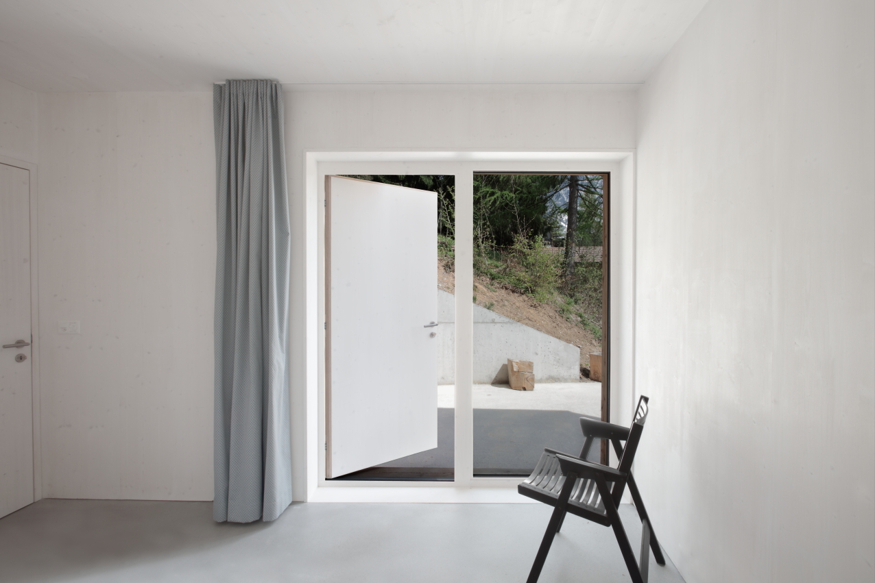 En Chalméry House by Christian Dupraz Architects — A minimalist interior threshold framed by floor-to-ceiling glazed doors with dark steel mullions.