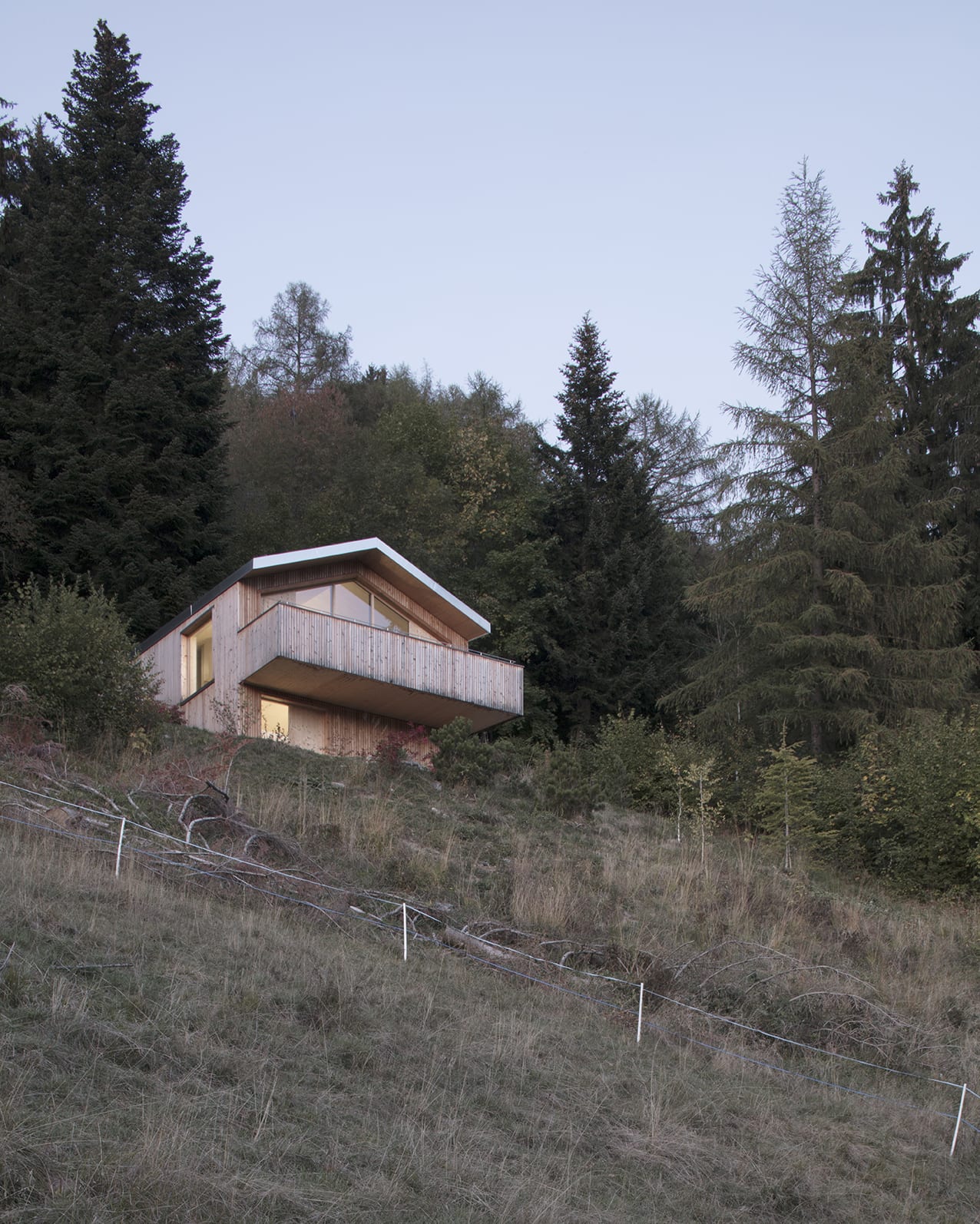 En Chalméry House by Christian Dupraz Architects — En Chalméry House sits elevated on a sloped Alpine terrain, its timber-clad form anchored by a dramatic cantilevered concrete platform.