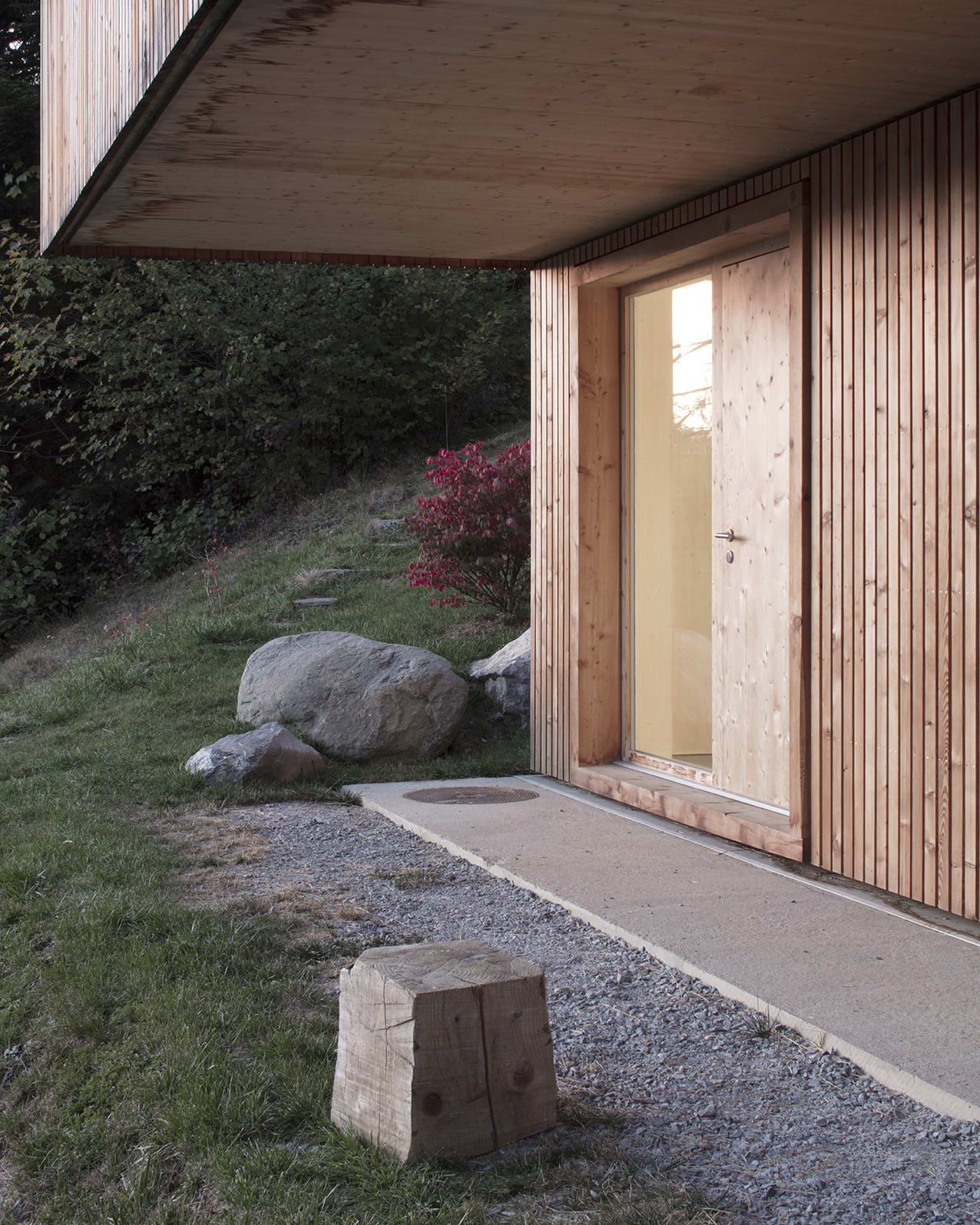 En Chalméry House by Christian Dupraz Architects — The entrance threshold frames a transition between exterior gravel terrace and interior cream-rendered wall.