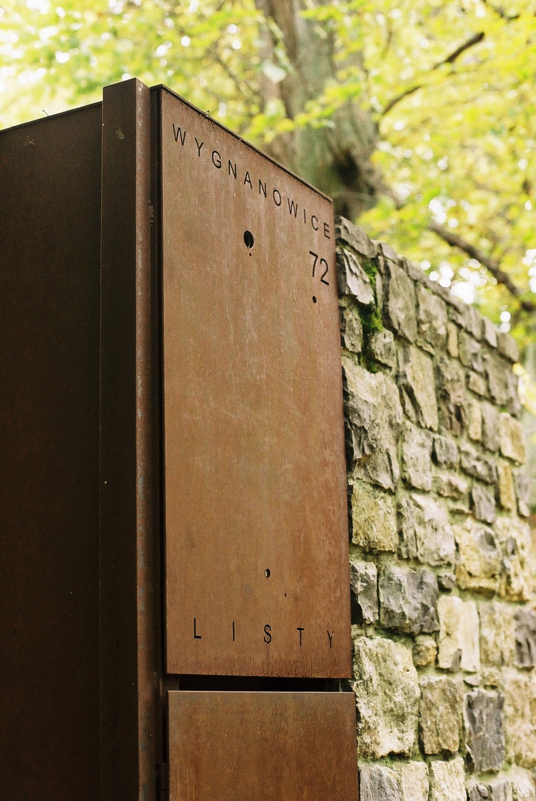 Wygnanowice House Over Crystal Clear Springs captured by Thisispaper Studio — A detail photograph of the entrance to Wygnanowice House capturing the wooden door frame and adjacent stone masonry.