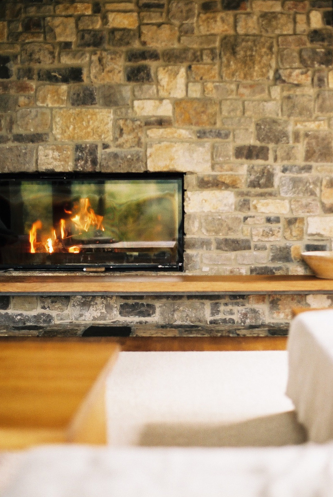 Wygnanowice House Over Crystal Clear Springs captured by Thisispaper Studio — Interior view of the fireplace installation within Wygnanowice House, featuring a modern recessed wood-burning stove set into coursed dolomite stone masonry.