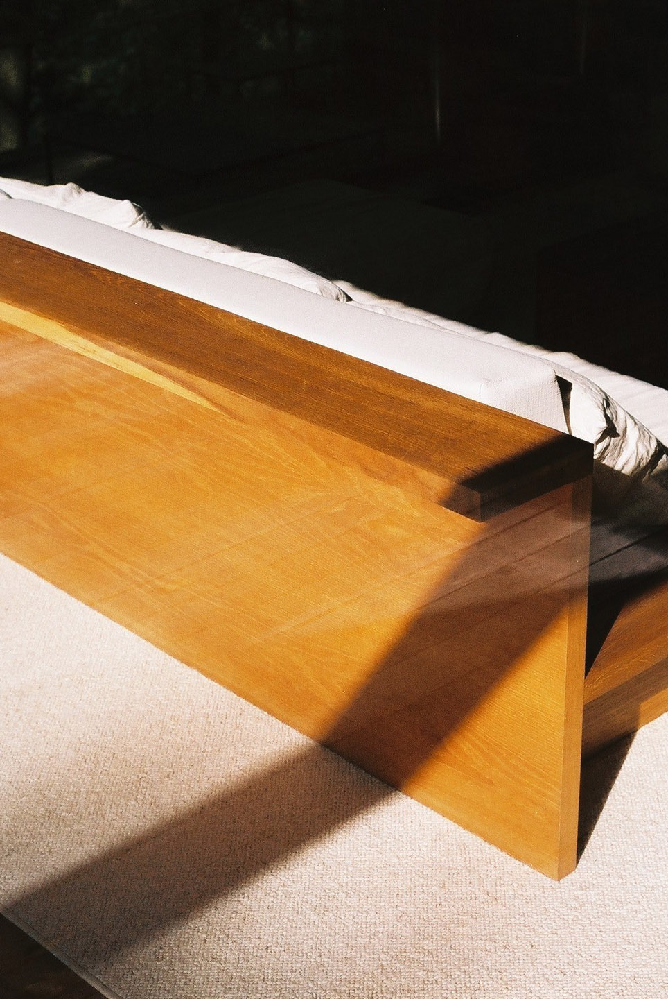 Wygnanowice House Over Crystal Clear Springs captured by Thisispaper Studio — A wooden bench with honey-toned oak grain catches afternoon sunlight streaming across a light linen upholstered surface.