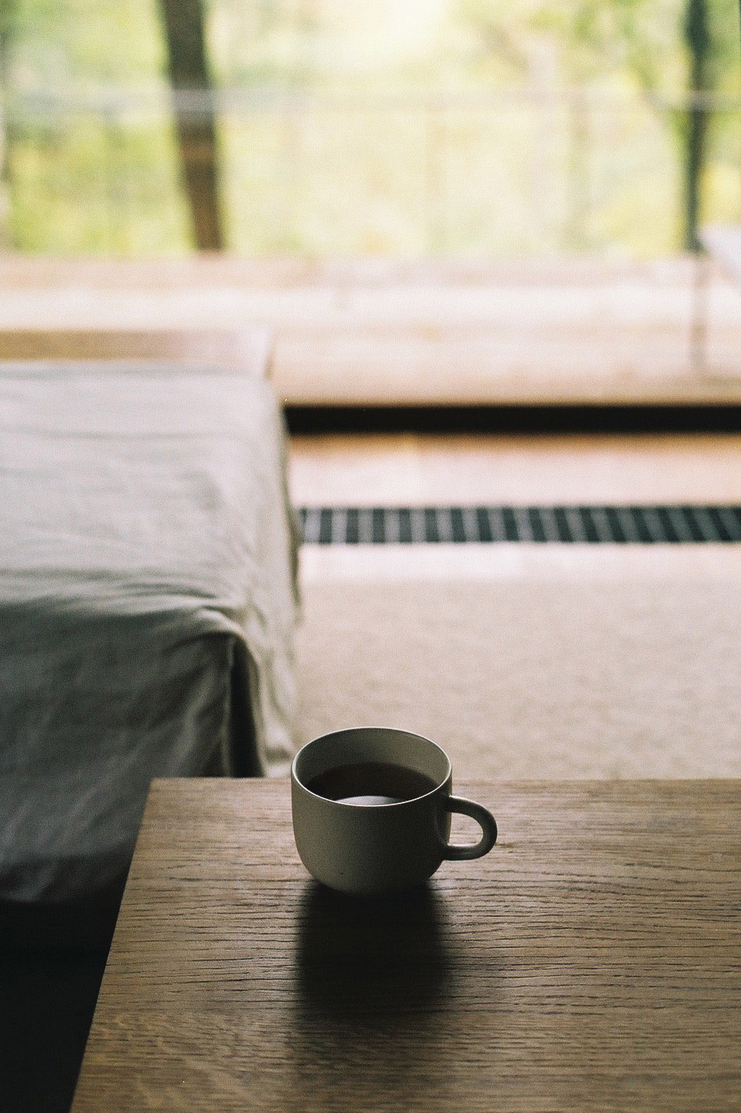 Wygnanowice House Over Crystal Clear Springs captured by Thisispaper Studio — A ceramic mug containing dark liquid sits on a wooden table in sharp focus, casting a subtle shadow across the grain surface.