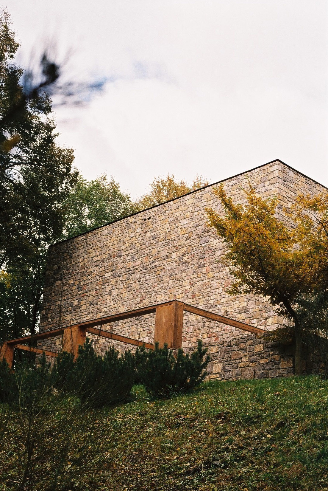 Wygnanowice House Over Crystal Clear Springs captured by Thisispaper Studio — A cubic stone structure anchors the composition, its coursed dolomite masonry displaying warm ochre and grey tones characteristic of Polish vernacular building.