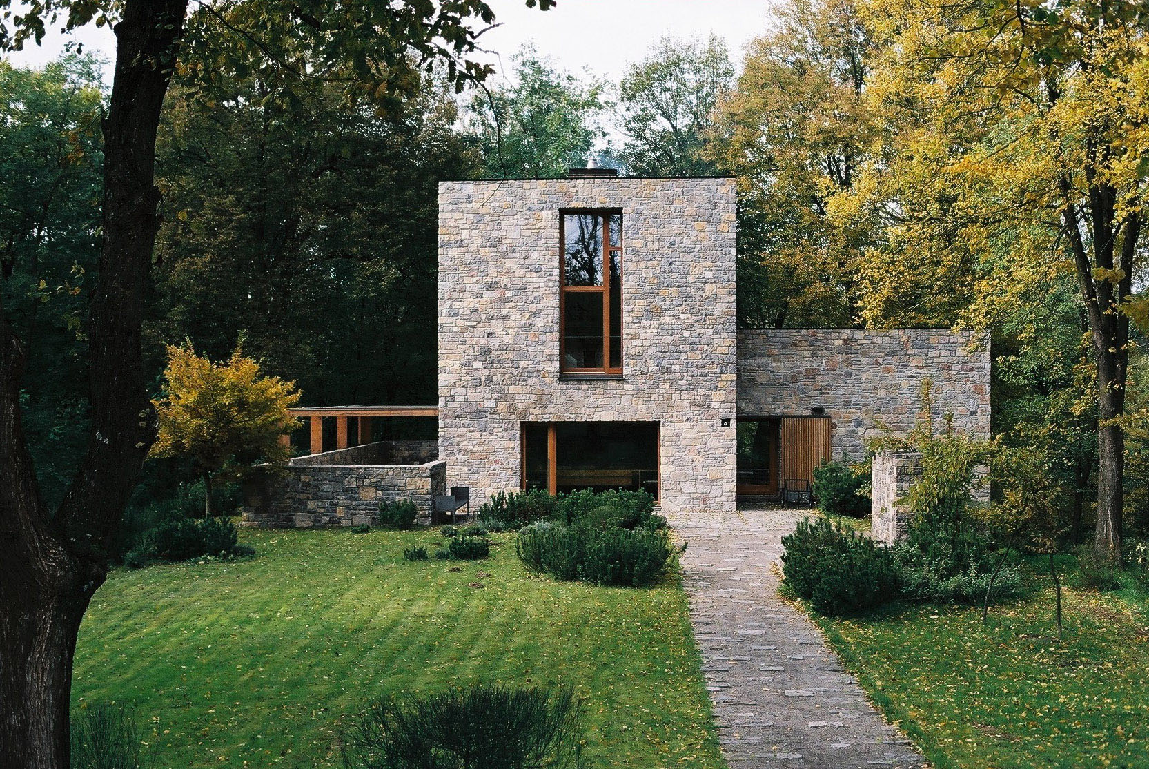 Wygnanowice House Over Crystal Clear Springs captured by Thisispaper Studio — A coursed dolomite stone tower rises from the Wygnanowice landscape, its pale ochre and grey masonry articulated against dense autumn foliage.