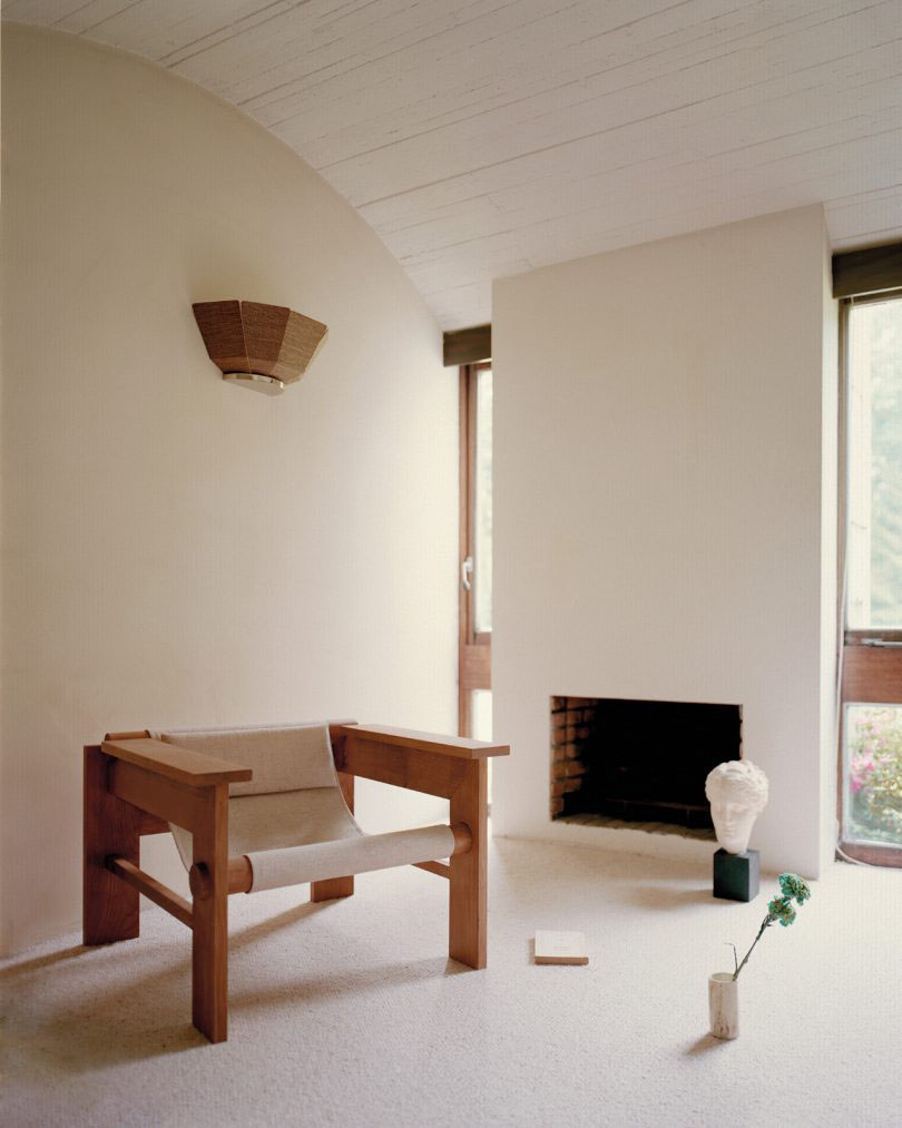 Furniture Collection by HAOS — A timber-framed lounge chair with exposed joinery at corner intersections and horizontal armrests dominates the foreground of this minimalist interior.
