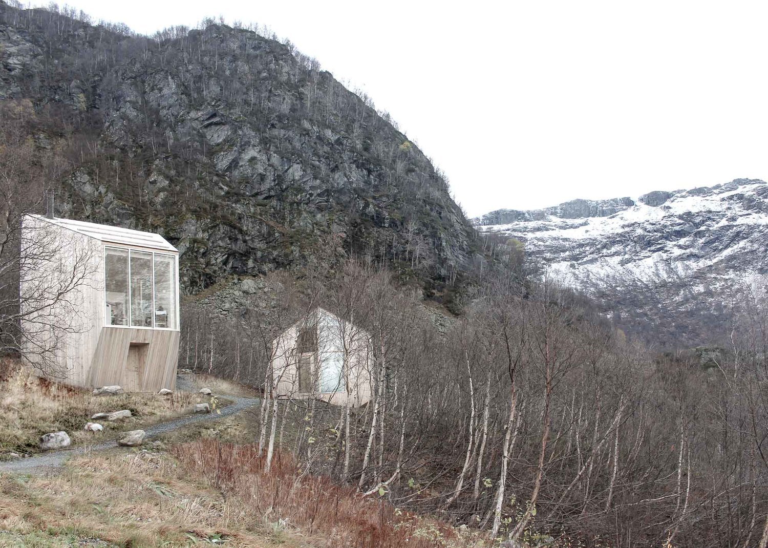 Røldal Cabin by Reiulf Ramstad Arkitekter — The Røldal Cabin's upper volume dominates the frame, its three-panel glazed window system spanning the full width of weathered timber cladding.