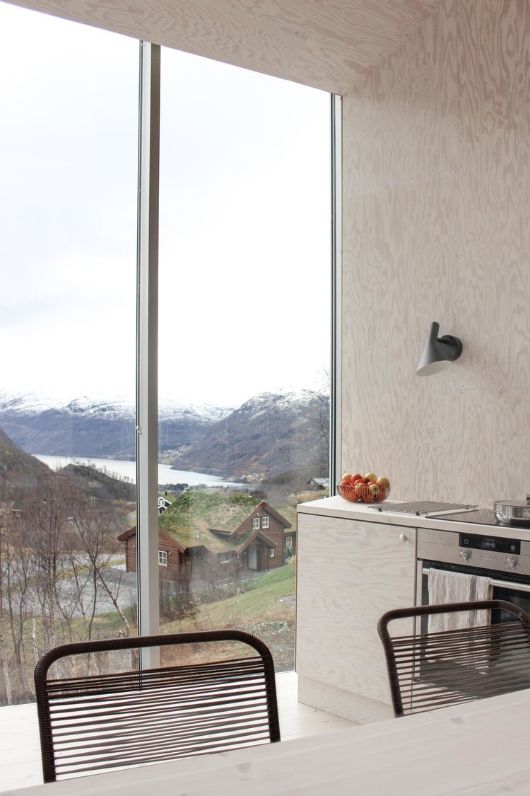 Røldal Cabin by Reiulf Ramstad Arkitekter — A kitchen interior framed by a three-panel glazed window system spanning the full width of the upper volume.