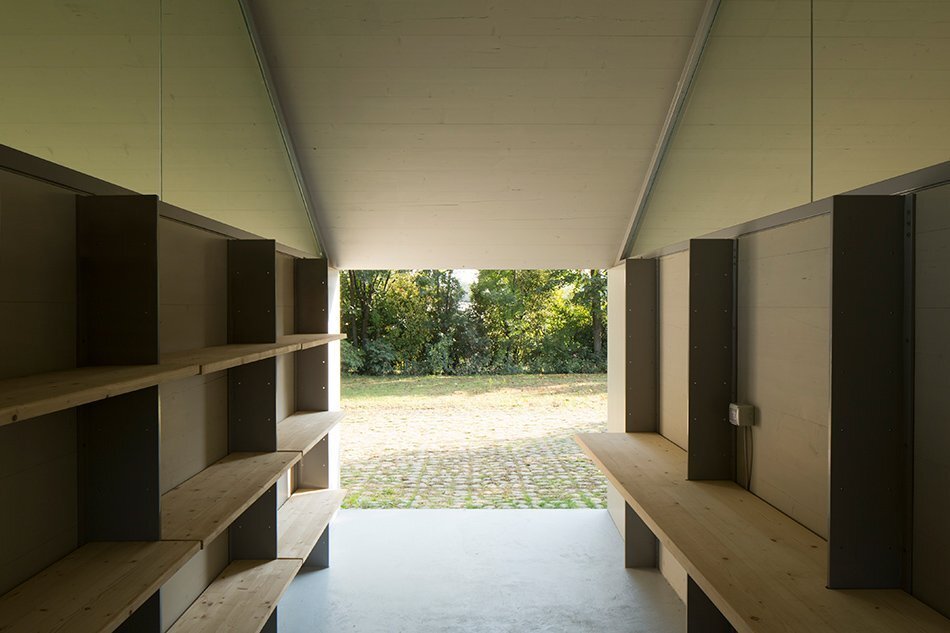 Garage and Workshop by Studiospazio — Interior view of the workshop space reveals the skeletal timber frame structure supporting the pitched gable roof.