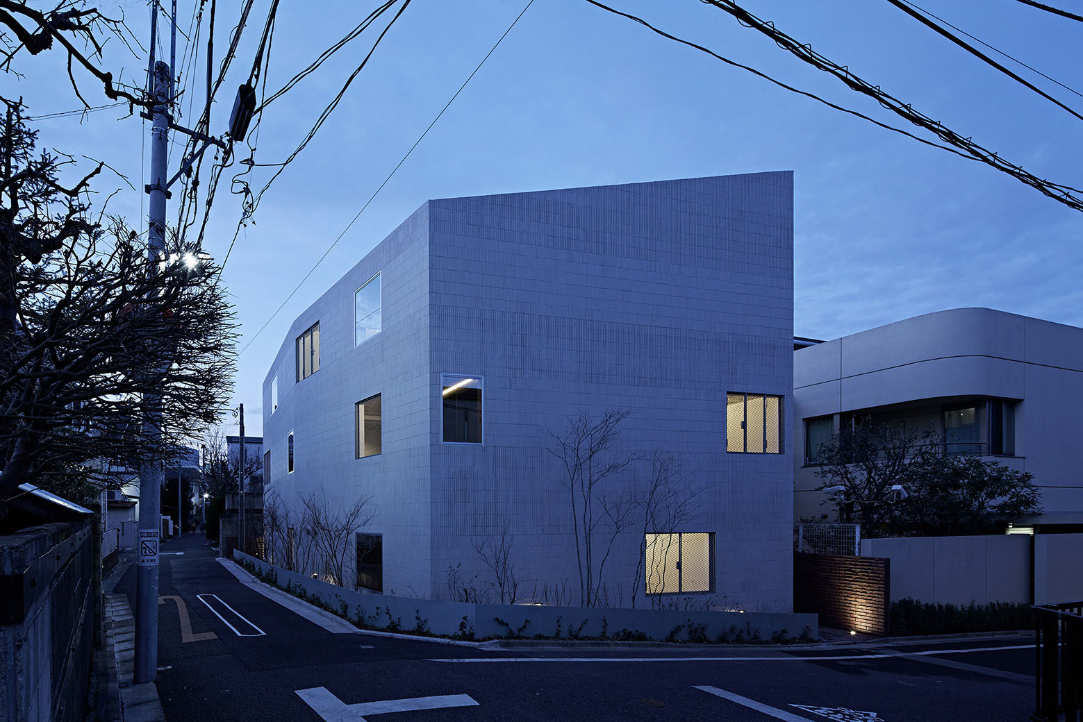 Oggi by Makoto Yamaguchi Design — Oggi House presents a monolithic concrete apartment building clad in white ceramic tile, its facade organized by a regular grid pattern interrupted by three...