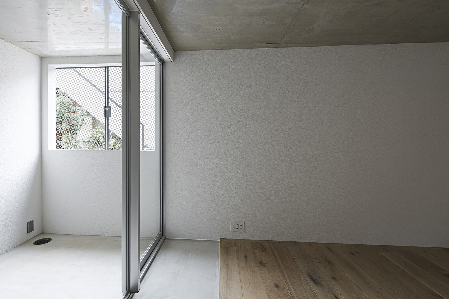 Oggi by Makoto Yamaguchi Design — Interior view of a residential unit featuring a sliding glass door system with dark aluminum framing that opens onto a covered balcony.