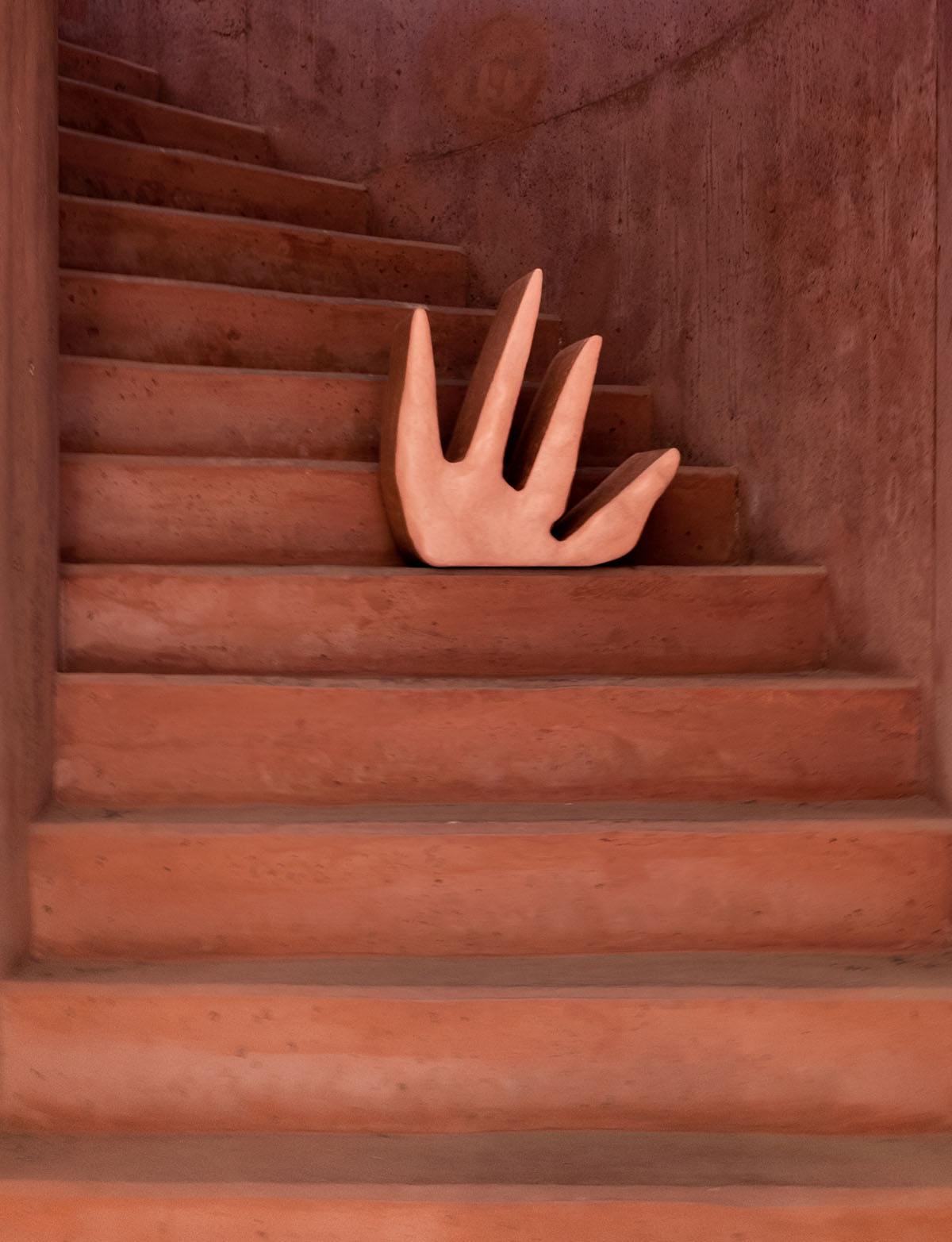 Roommates by Barbora Žilinskaite — A hand-sculpted composite form positioned on a wooden staircase depicts an abstracted human torso with four columnar legs emerging from a flat rectangular base.