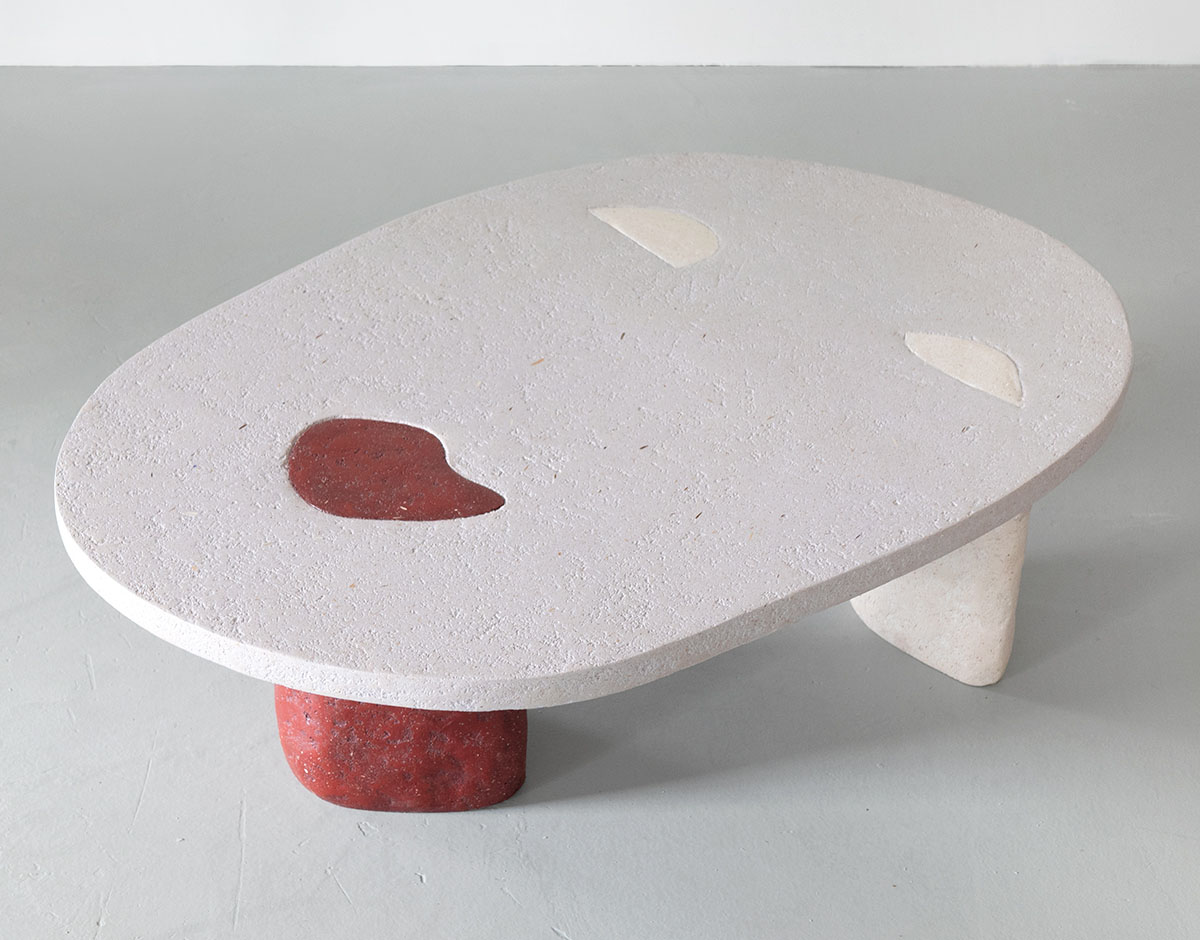 Roommates by Barbora Žilinskaite — A sculptural table with an oval white composite top surface featuring two cutout voids and dark red pigmentation visible through one opening.