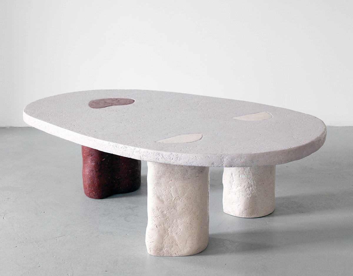 Roommates by Barbora Žilinskaite — A sculptural table with an elliptical top surface, supported by three cylindrical legs of varying heights in cream-colored composite material.