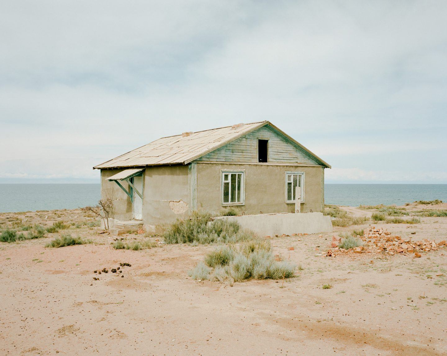 Horsehead Nebula by Matthieu Litt — A single-storey residential structure occupies an expansive arid landscape bordering a calm sea horizon.