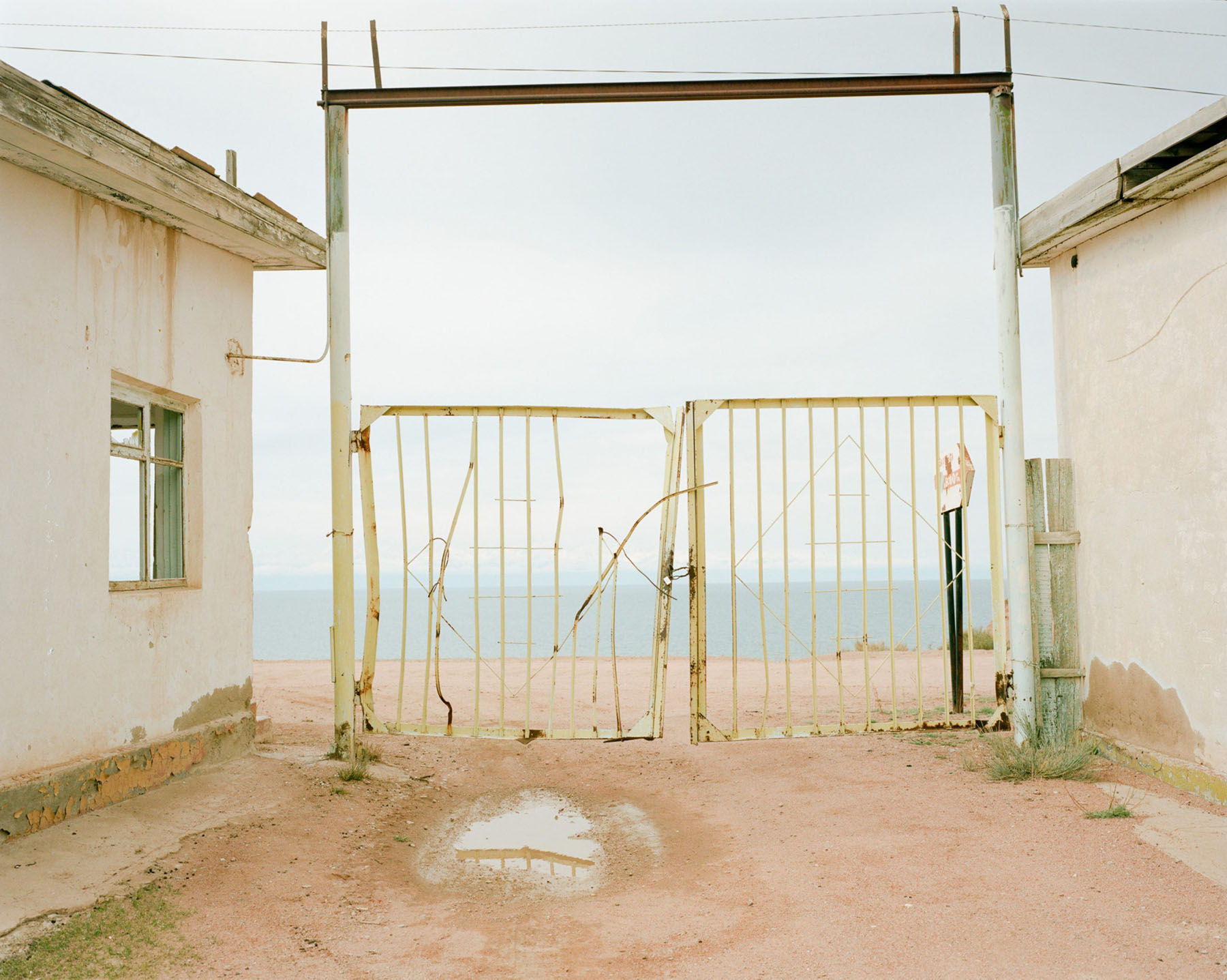 Horsehead Nebula by Matthieu Litt — Matthieu Litt photographs a deteriorated coastal structure in Faristan, Central Asia, where two whitewashed concrete buildings frame a corroded metal gate.