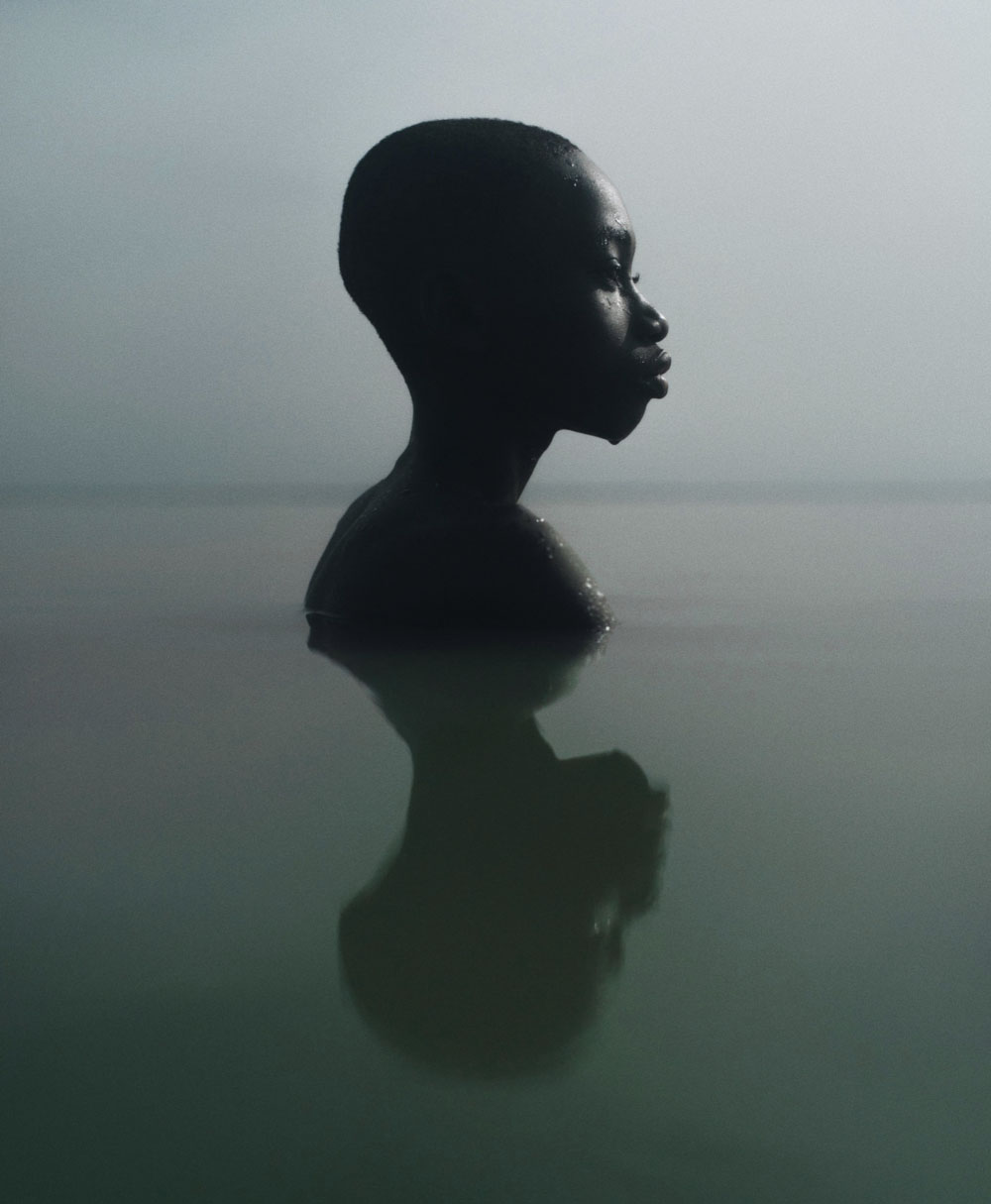Selected works by Jeremy Snell — A figure submerged to chest level in still water, captured in profile silhouette against an overcast, pale sky.