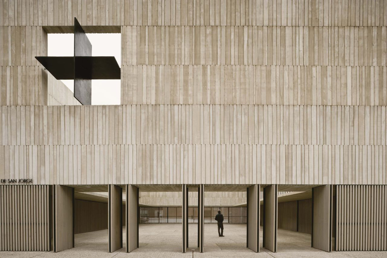 San Jorge Church by Tabuenca & Leache — The San Jorge Church facade presents a composed grid of vertical timber slats in warm beige tones, interrupted by a singular geometric aperture.