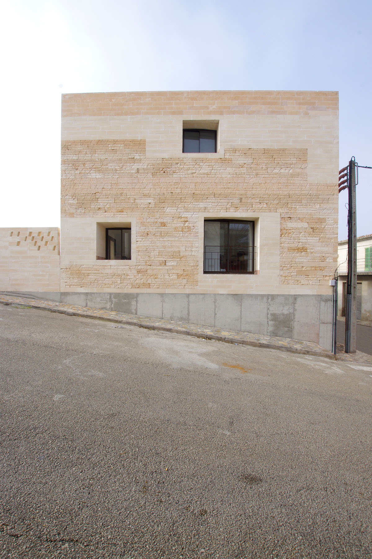 Jordi and África's House by TEd’A arquitectes — The corner facade of Jordi and África's House presents marés sandstone ashlar in horizontal courses, its pale honey tone interrupted by a geometric grid of...