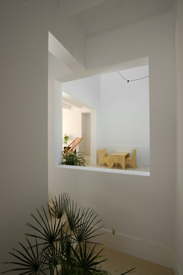 Jordi and África's House by TEd’A arquitectes — A recessed window opening frames an interior room rendered in white plaster and concrete, creating a layered threshold between spaces.