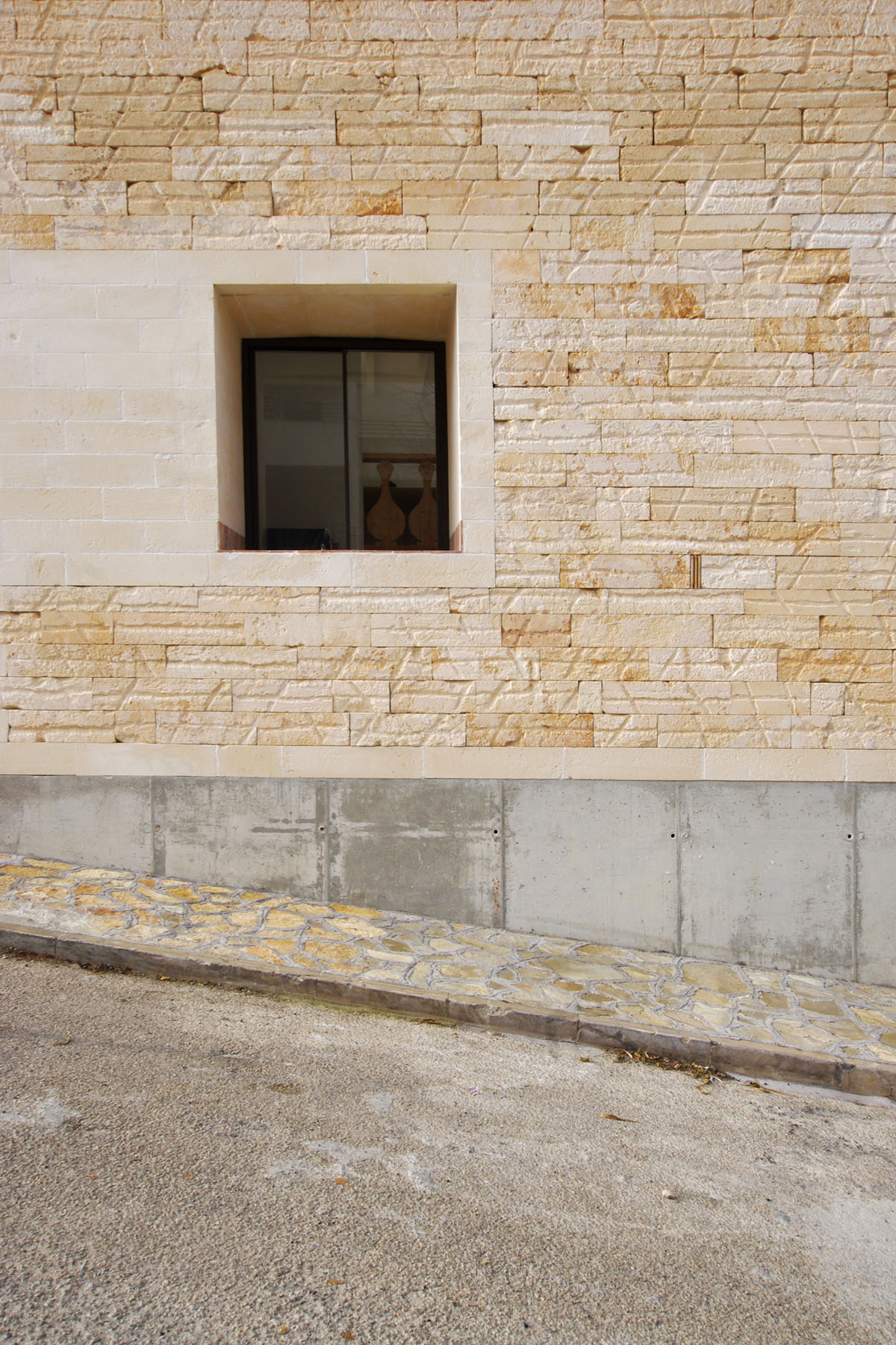 Jordi and África's House by TEd’A arquitectes — A pale sandstone ashlar facade dominates this elevation, its rectangular blocks laid in regular horizontal courses with subtle ochre and cream variations.