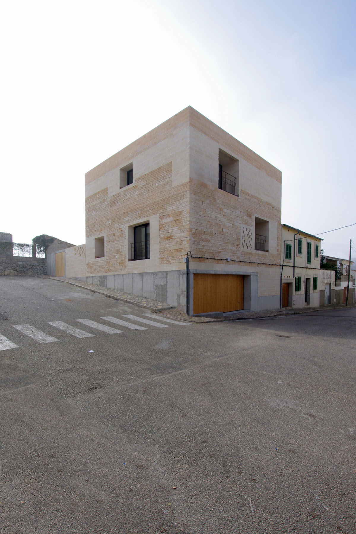 Jordi and África's House by TEd’A arquitectes — A corner residential structure clad in pale sandstone ashlar blocks laid in horizontal courses, anchoring a rural Majorcan street.
