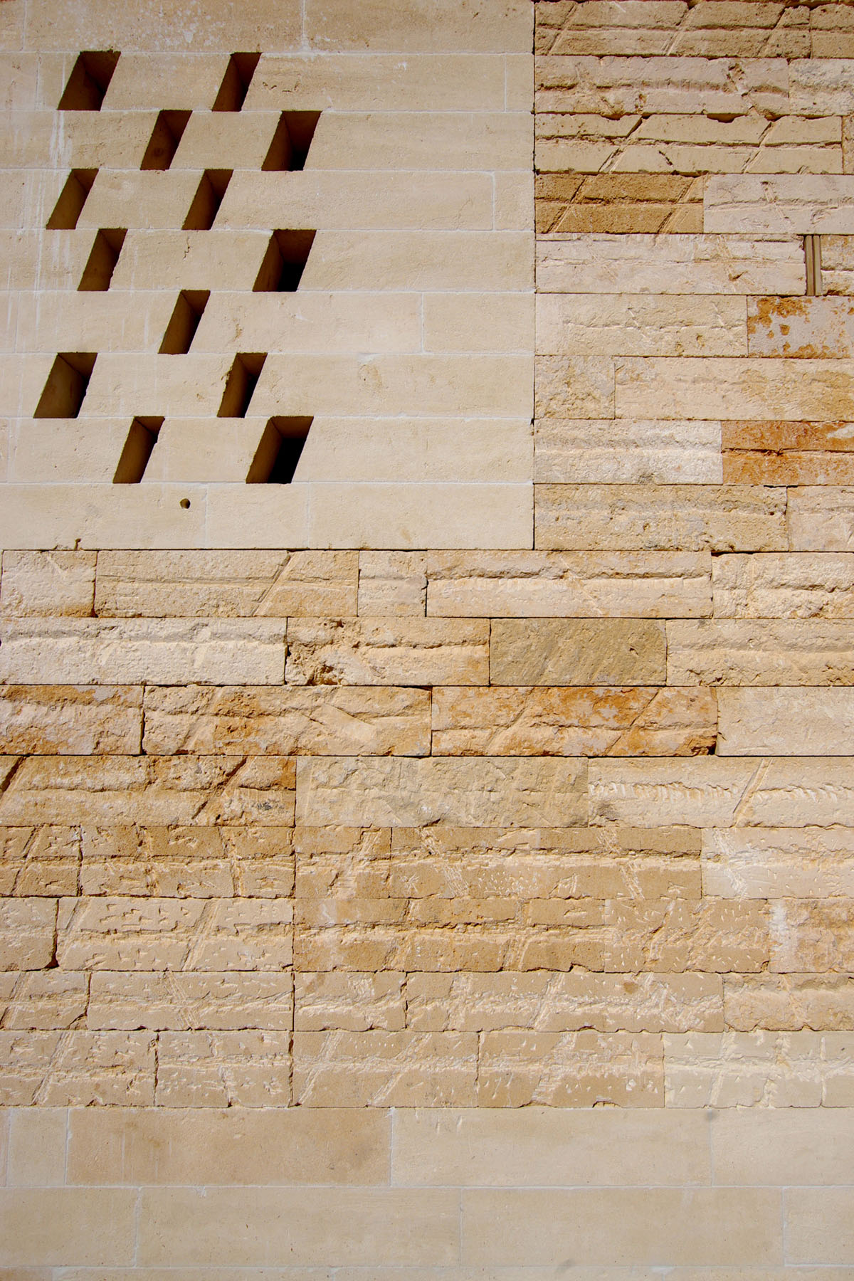 Jordi and África's House by TEd’A arquitectes — Detail of the marés stone façade showing the distinctive diagonal pattern of rectangular perforations cut through pale sandstone ashlar blocks.