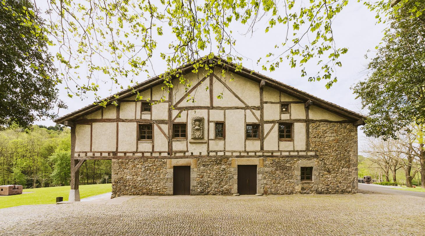 Eduardo Chillida Leku Museum — A half-timbered structure with rendered infill panels rises above a stone-built base, its timber frame members clearly articulated against cream-colored walls.