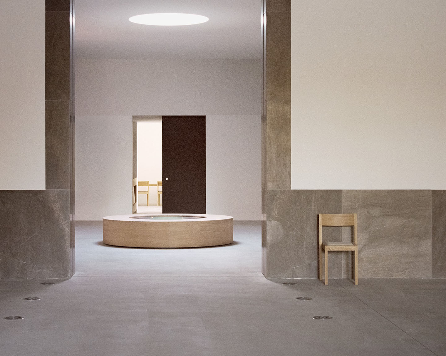 Loenen Pavilion by KAAN Architecten — A recessed interior threshold frames a volumetric wooden counter positioned centrally beneath a circular skylight.