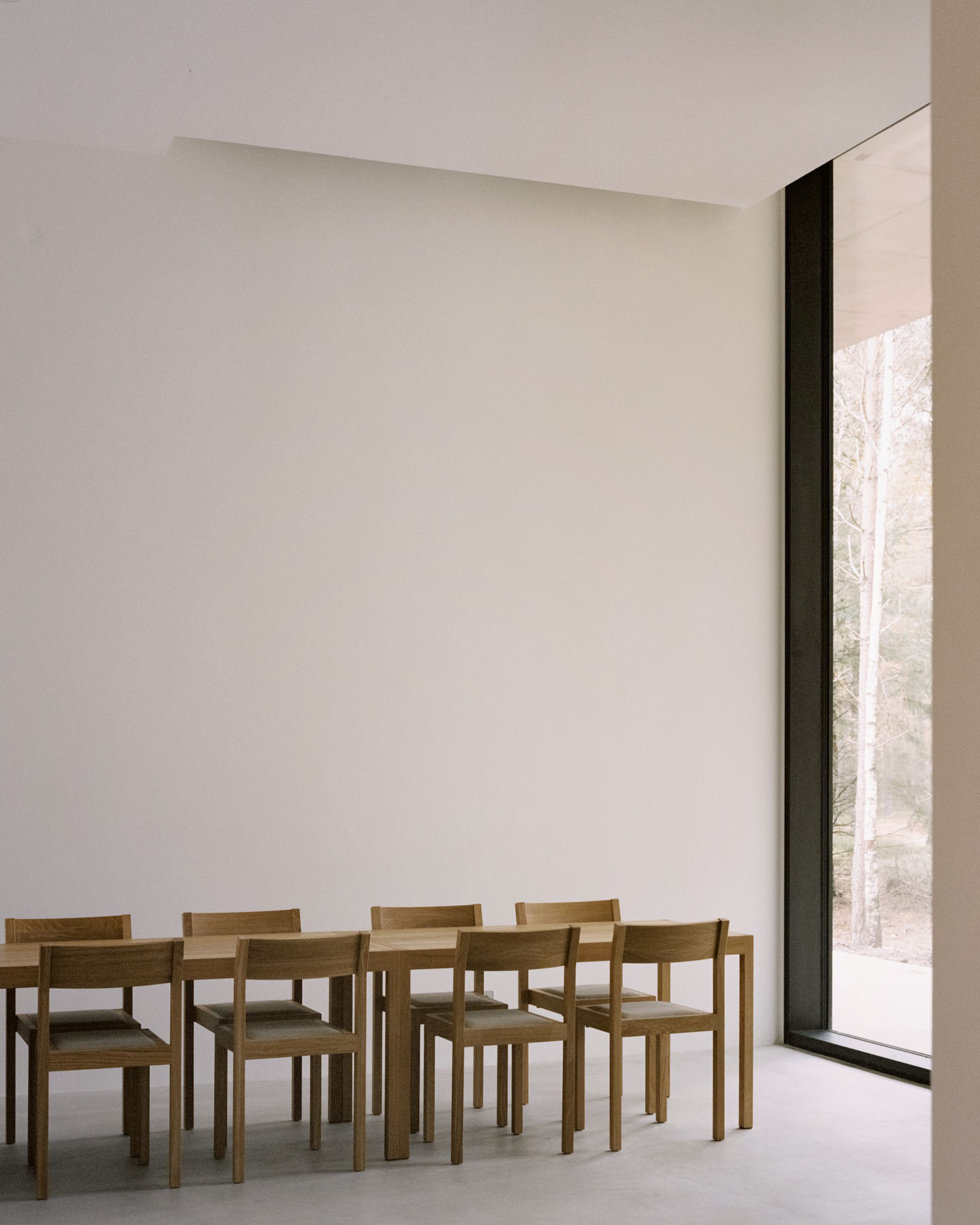 Loenen Pavilion by KAAN Architecten — Interior view of the Loenen Pavilion showing a dining arrangement of six wooden chairs positioned before a floor-to-ceiling glazed wall.