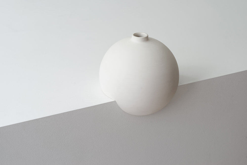 Tumble by Falke Svatun — A single cream slip-cast stoneware vessel with matte finish positioned on a white plaster platform bisected by a diagonal grey band.