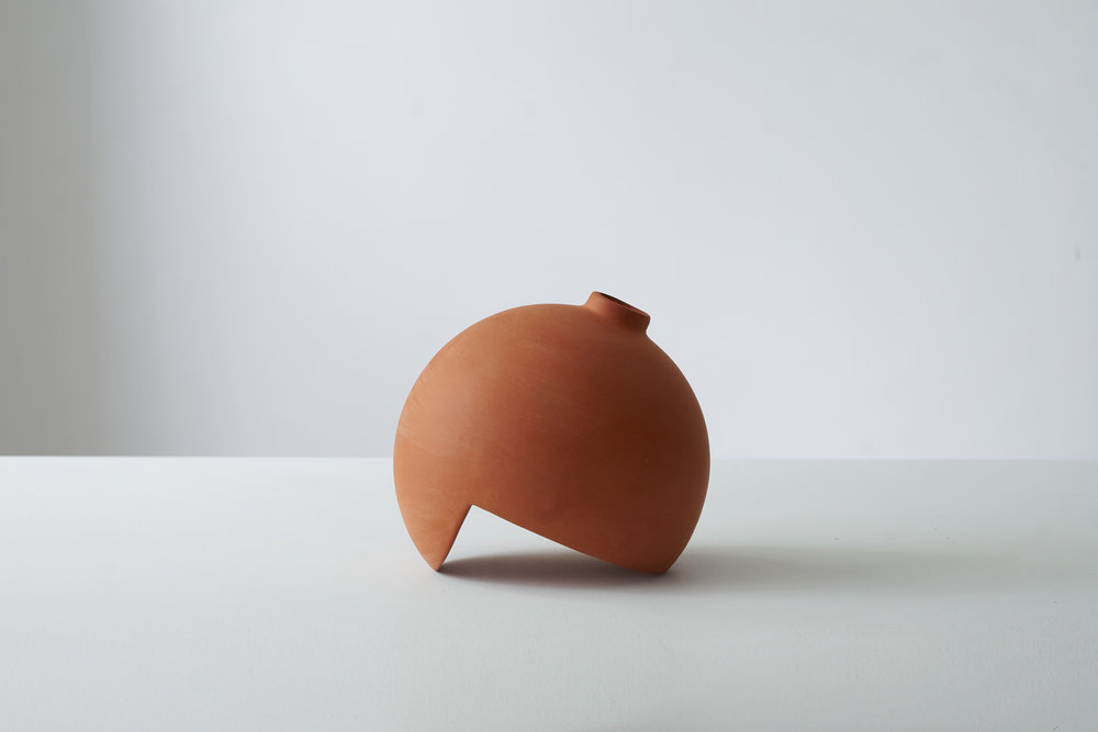 Tumble by Falke Svatun — A slip-cast stoneware vessel with terracotta matte finish occupies the center of a white plaster platform.