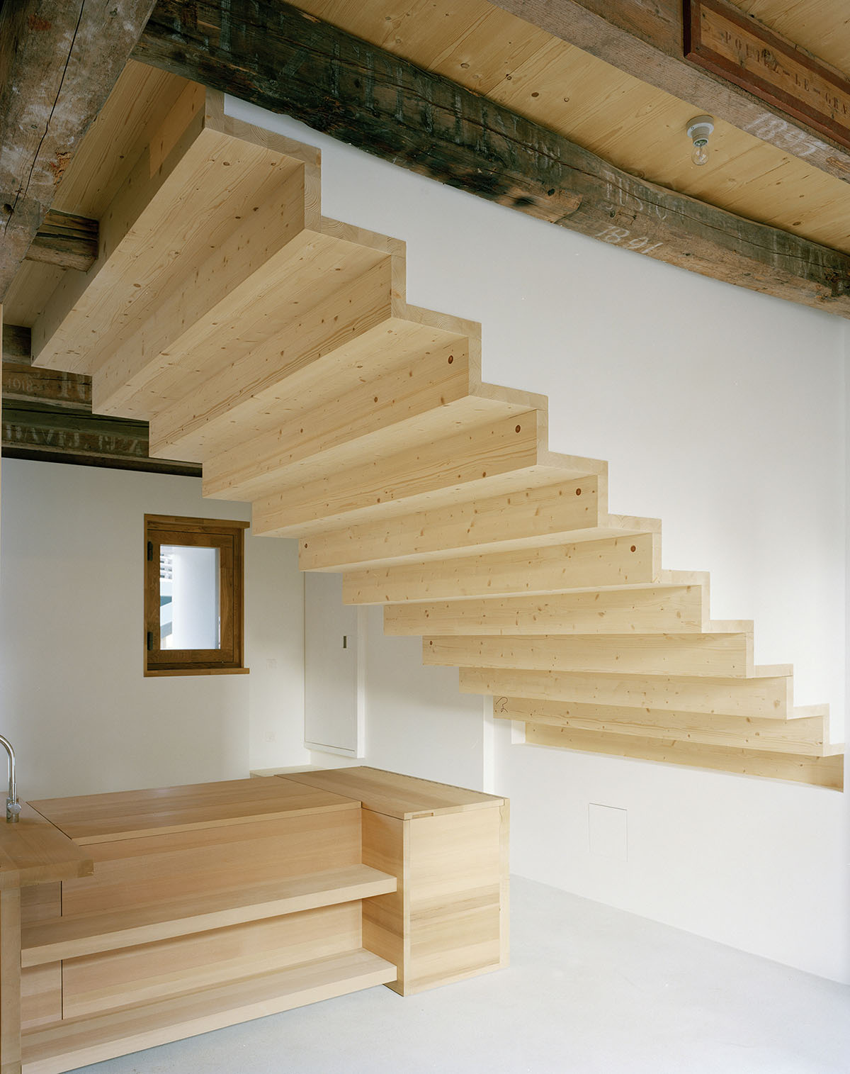 2 Houses in Chigny by Dieterdietz.org — Interior view of a timber stair ascending diagonally across a white wall, constructed from pale pine with visible knots and board grain.