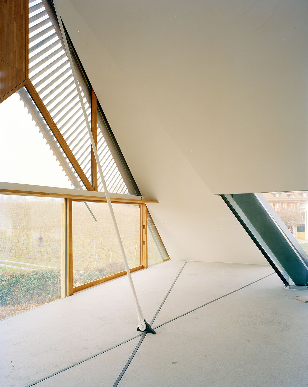 2 Houses in Chigny by Dieterdietz.org — A sloped attic space with pitched timber rafters and cream-colored plasterboard walls captures diffused daylight through angled skylights with white-painted...