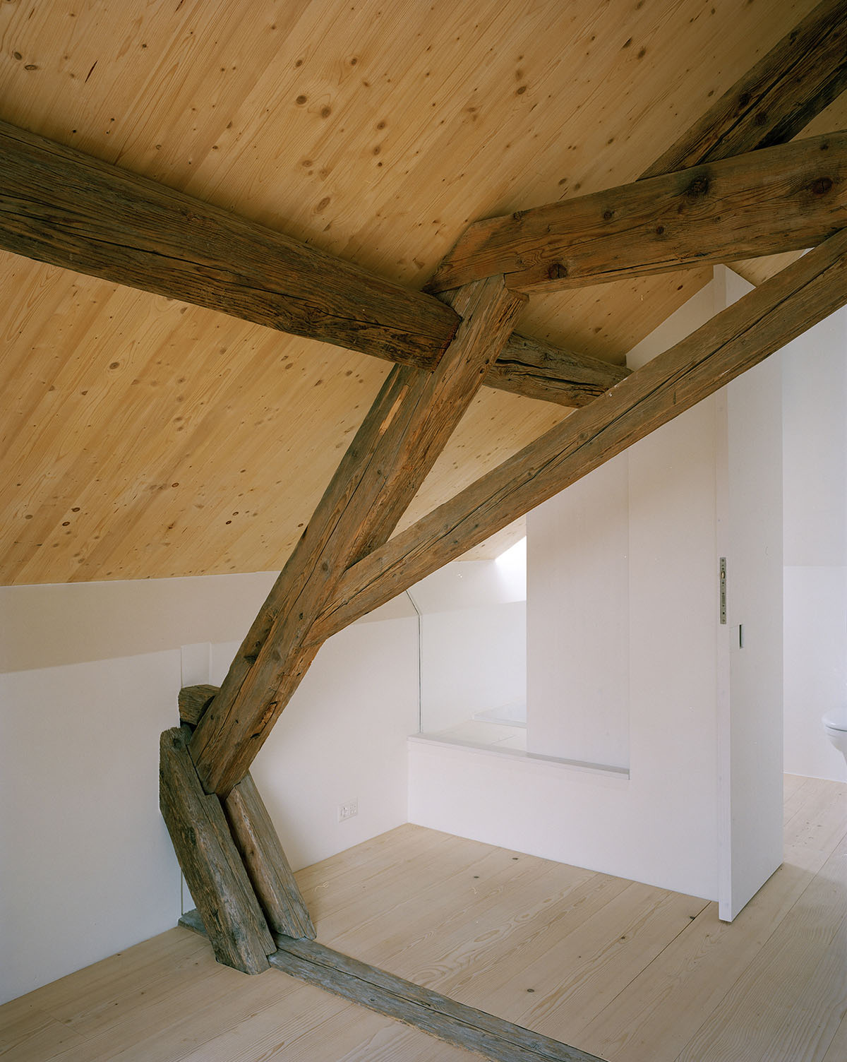 2 Houses in Chigny by Dieterdietz.org — Attic interior revealing the structural logic of the renovation: dark timber beams—likely salvaged or period-appropriate—intersect at sharp angles against a...