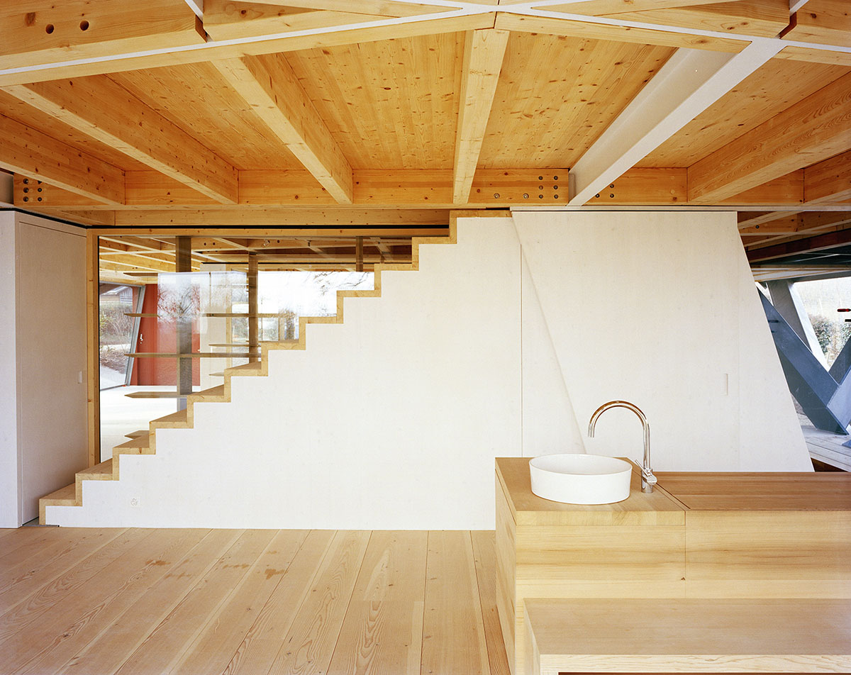 2 Houses in Chigny by Dieterdietz.org — Interior view of shared living space featuring exposed timber post-and-beam construction with white steel connecting elements.