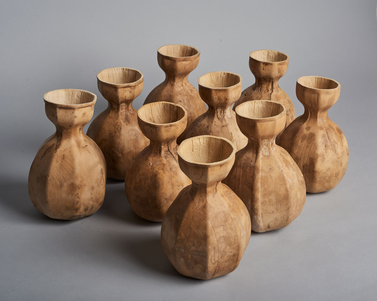 Biodegradable HyO-Cup by Crème — Nine hand-carved wooden vessels arranged in a clustered formation against a neutral gray background.