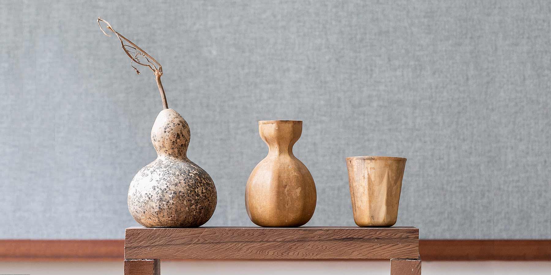 Biodegradable HyO-Cup by Crème — Three biodegradable gourd vessels arranged in descending height on a dark timber platform.