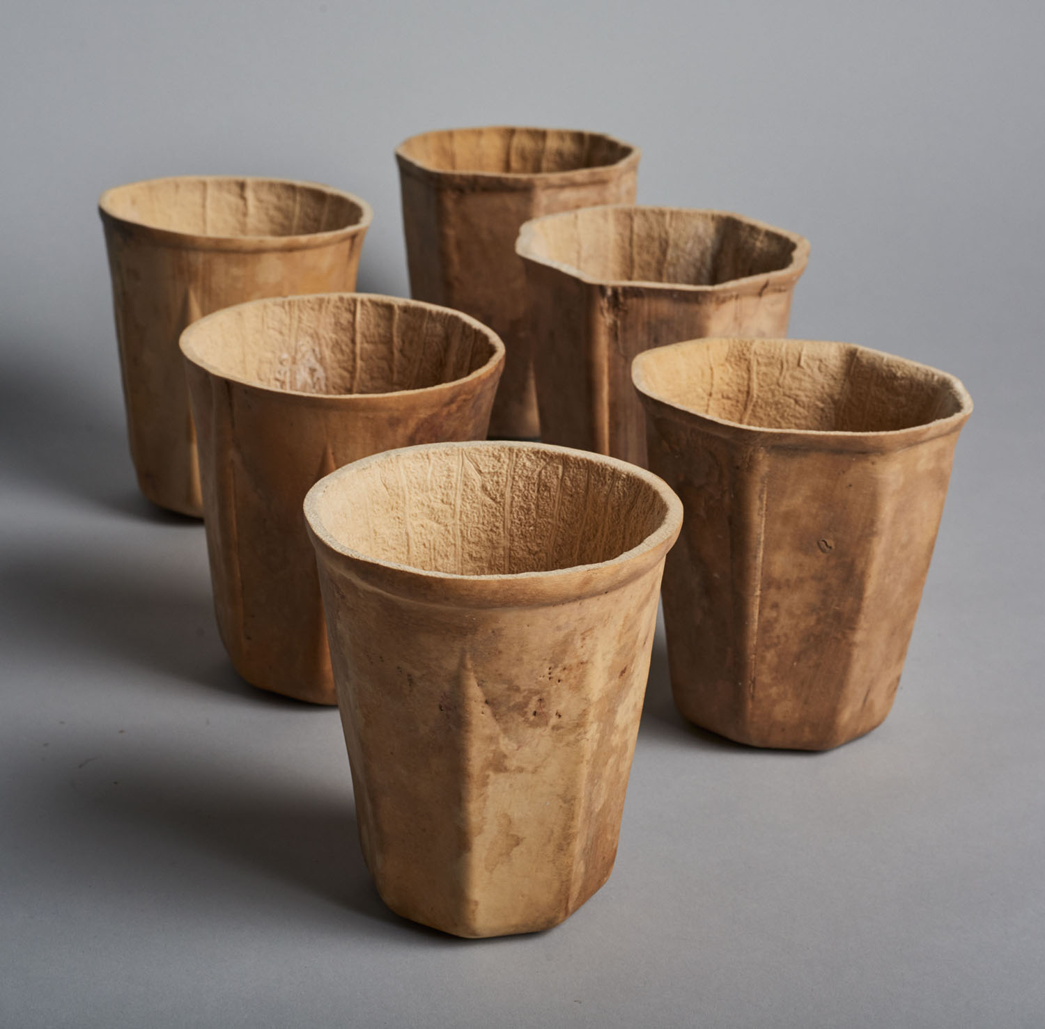 Biodegradable HyO-Cup by Crème — Six biodegradable gourd vessels arranged in a staggered formation against a neutral ground.