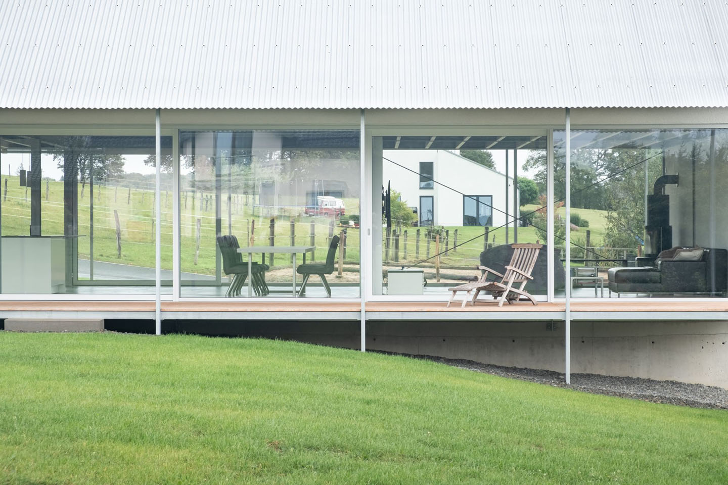 House D6 by Aretz Dürr Architektur — A horizontal glazed facade frames the pastoral landscape beyond, with large-format glass panels creating a permeable threshold between interior and exterior.