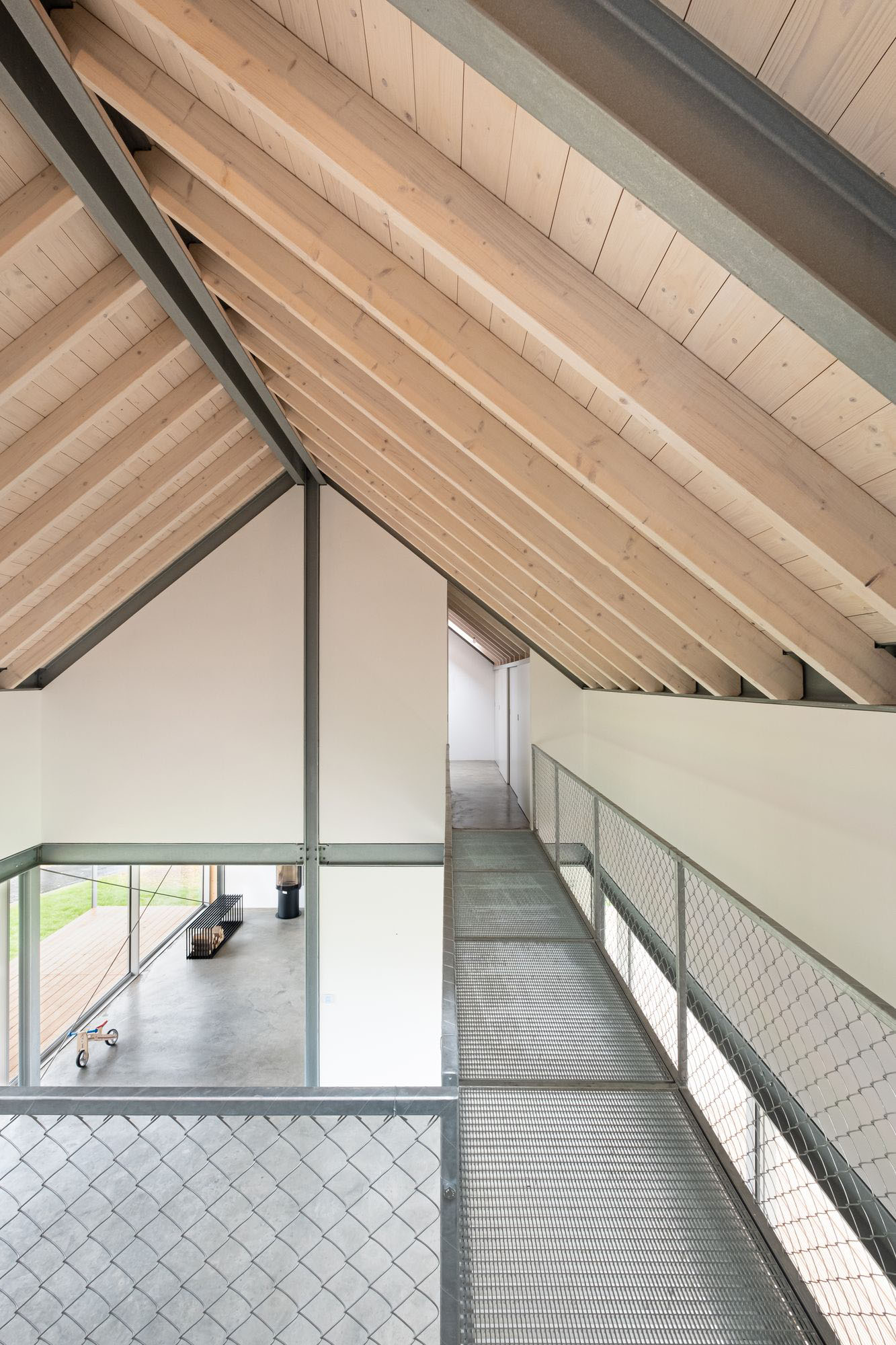 House D6 by Aretz Dürr Architektur — A mezzanine corridor frames the double-height living space below, where exposed timber beams span 5.4 metres at regular intervals across the pitched ceiling.